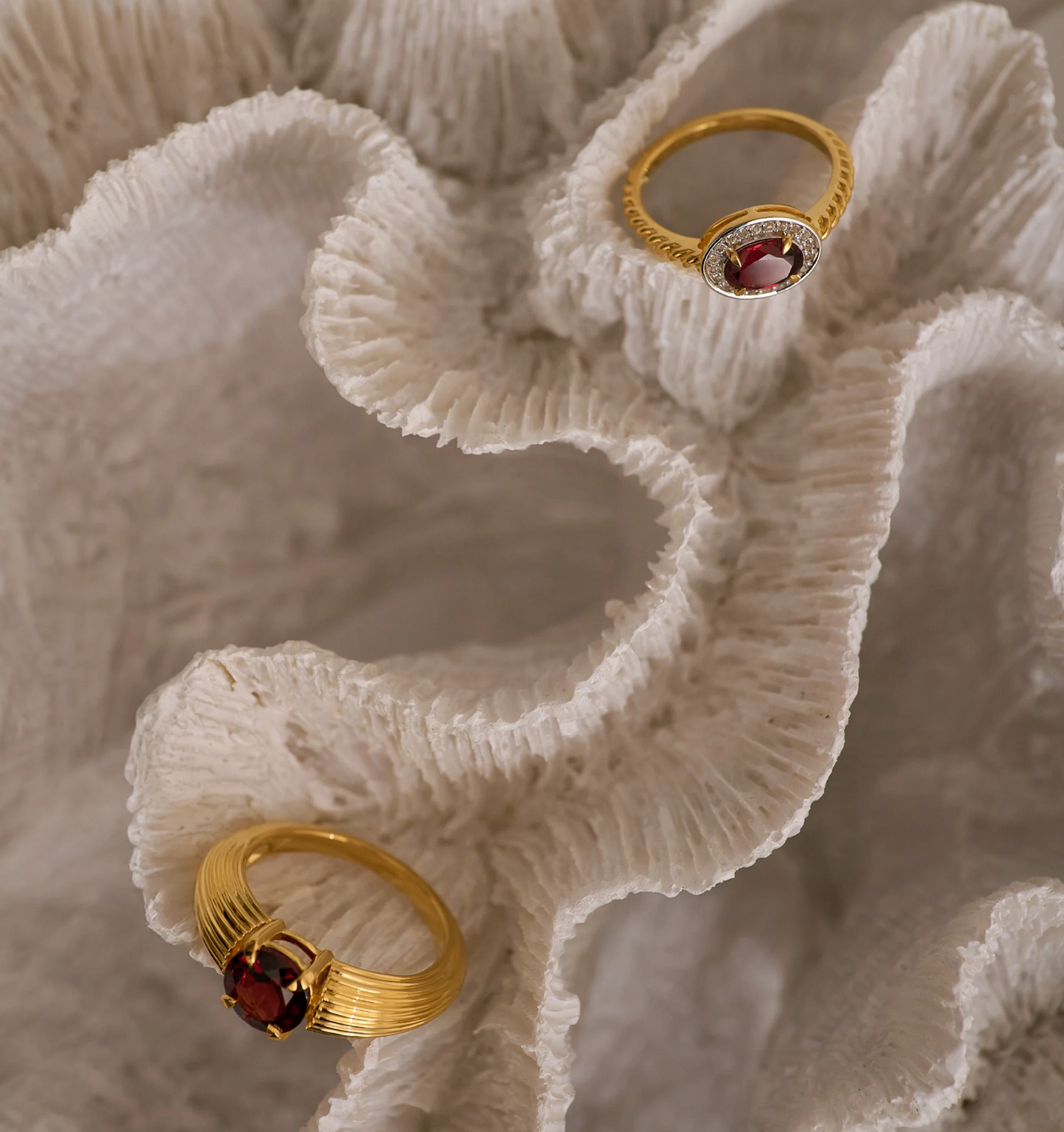 Agira Ring with garnet center and white topaz halo on gold band displayed on textured white surface