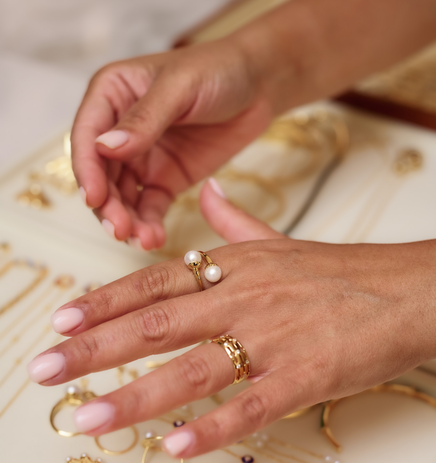 Close-up of hand wearing YugYagn Ring with two pearls and gold band against blurred jewelry background