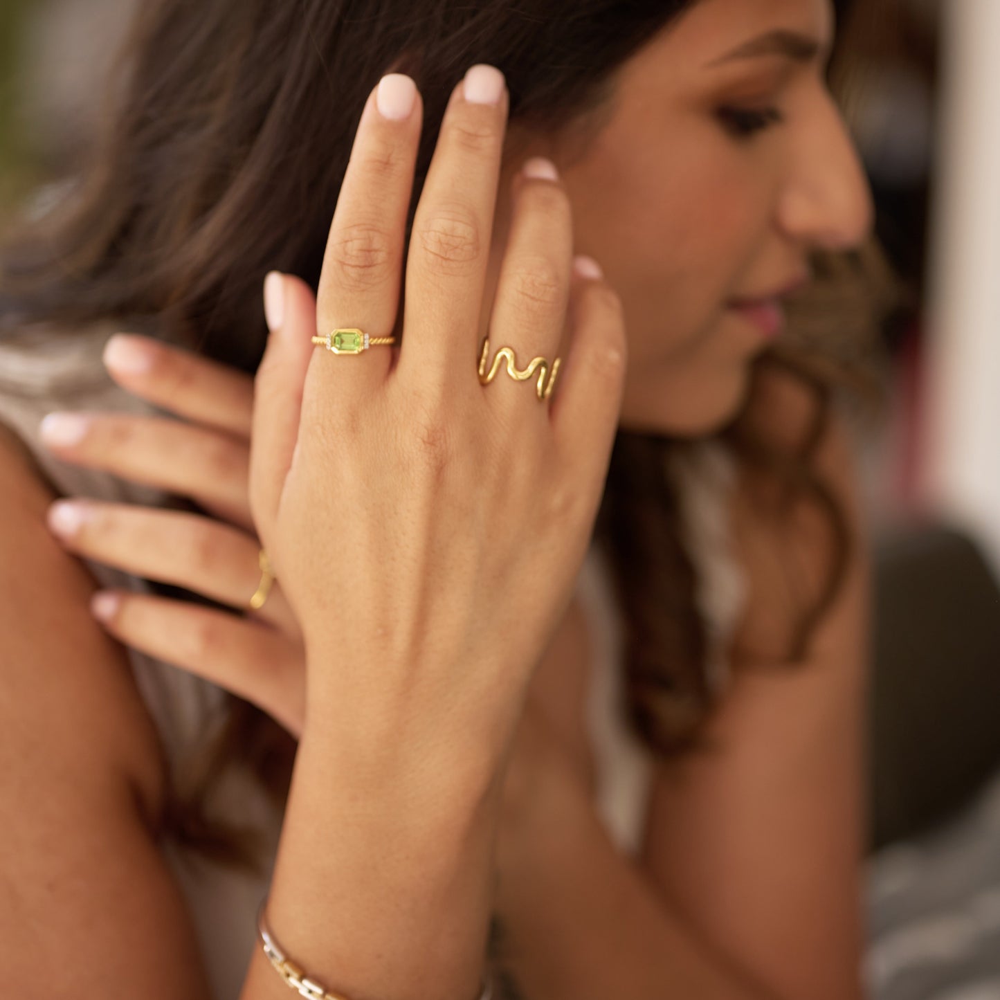 Close-up of a woman wearing a gold Solae Ring featuring a green peridot gemstone and white topaz accents.