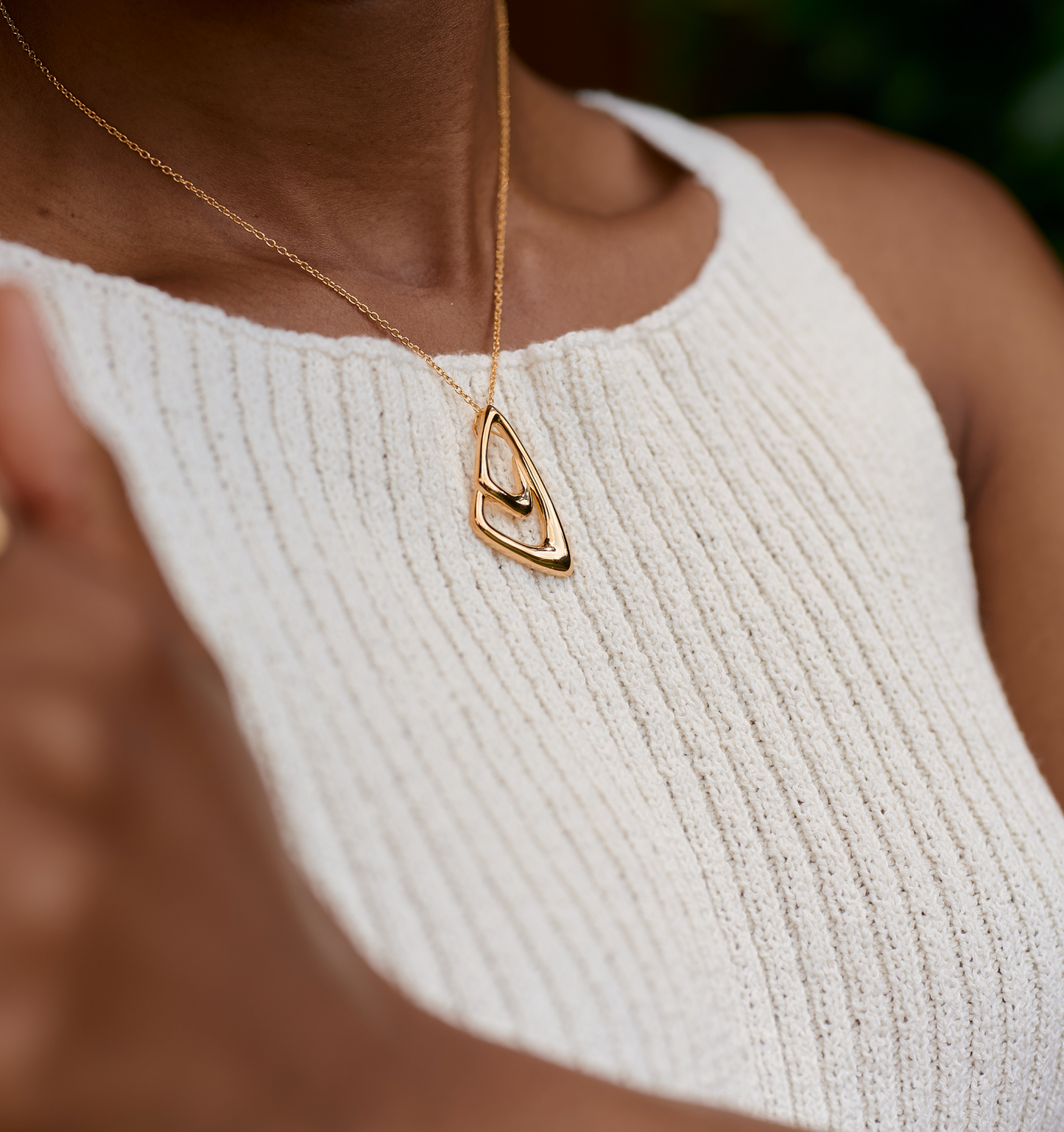 Aavrit Necklace elegant gold pendant with geometric curves on a delicate chain worn on a white textured top