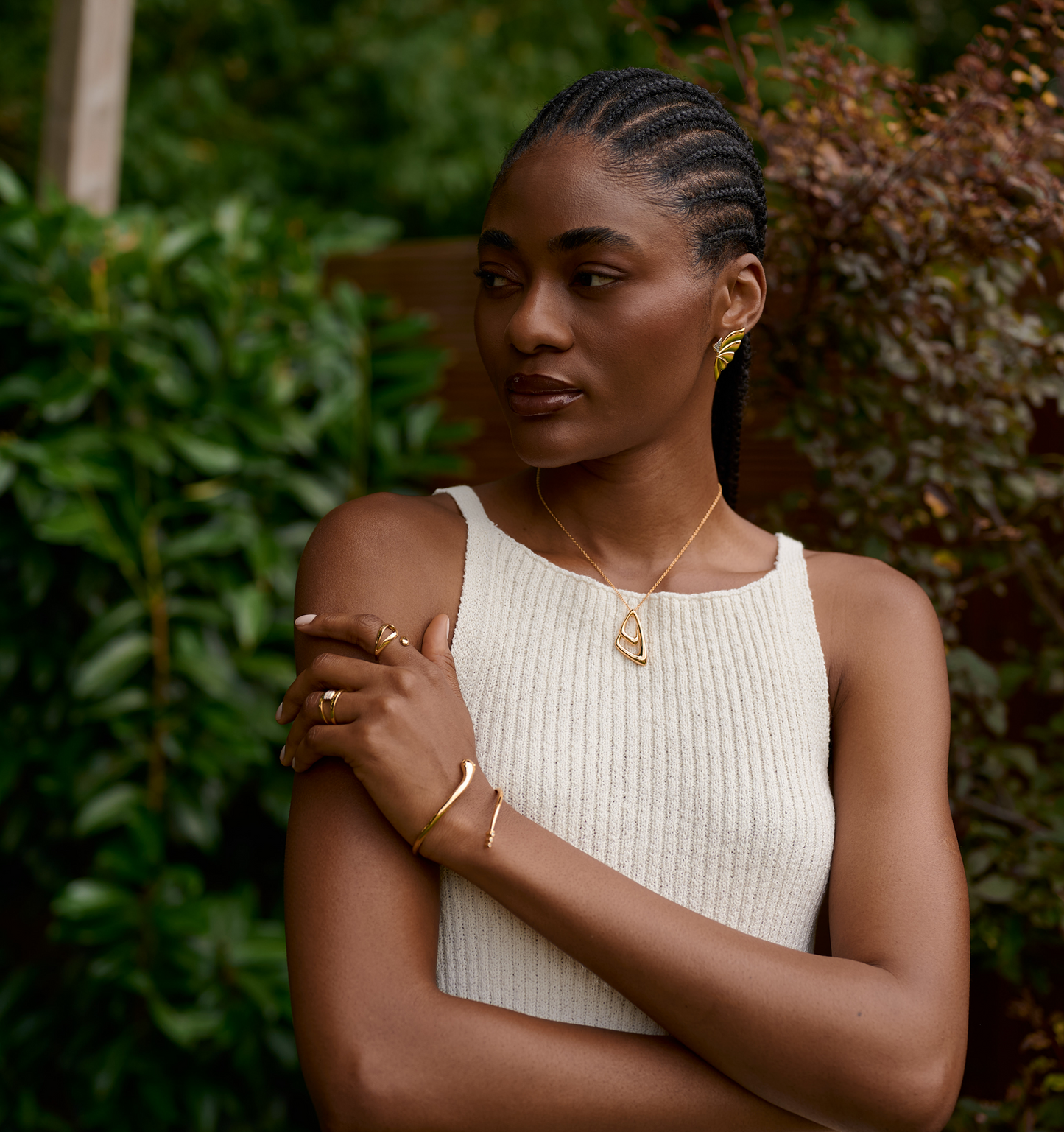 Woman wearing Aavrit Necklace with gold geometric pendant and matching gold jewelry outdoors
