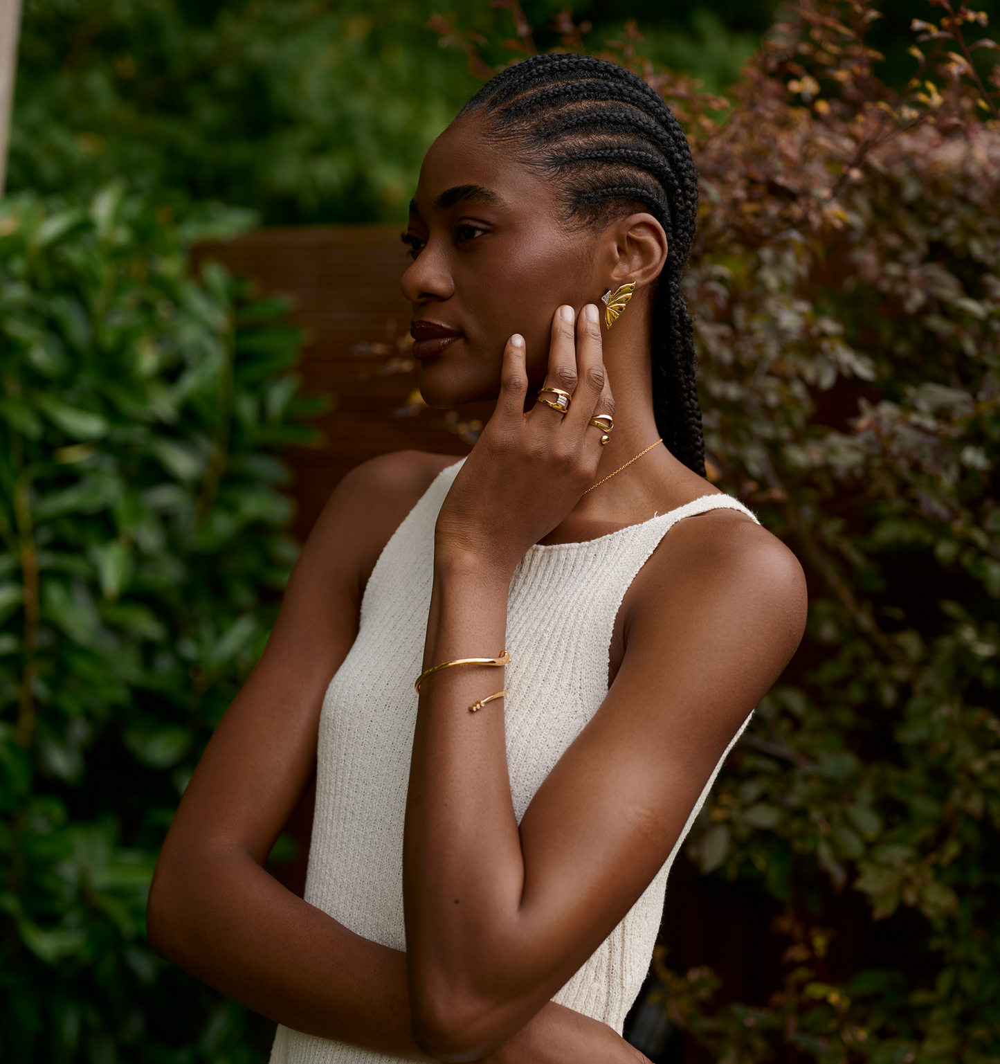Woman wearing layered gold Elara Earrings shaped like butterfly wings with matching gold rings and bracelet outdoors