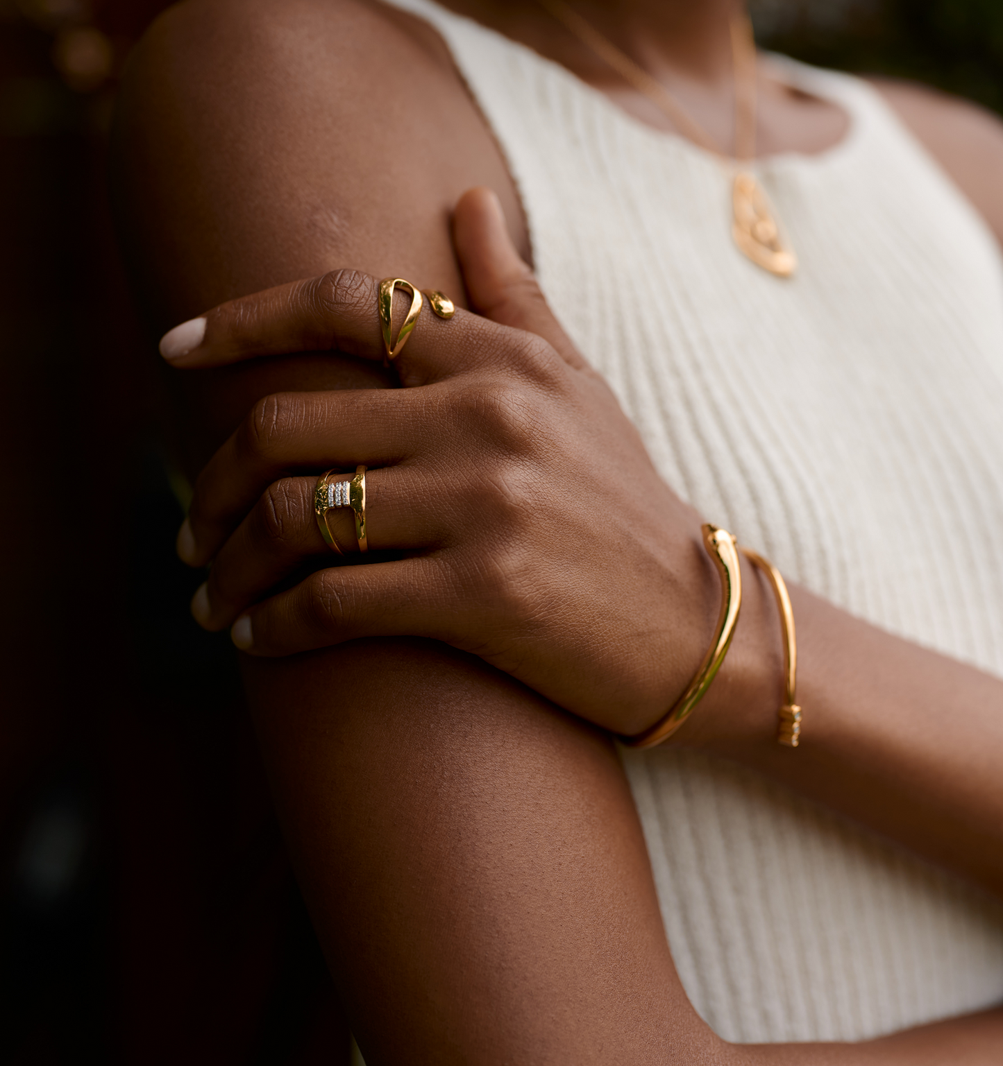 Close-up of hand wearing gold Setu Ring with white topaz, styled with gold bracelet and necklace