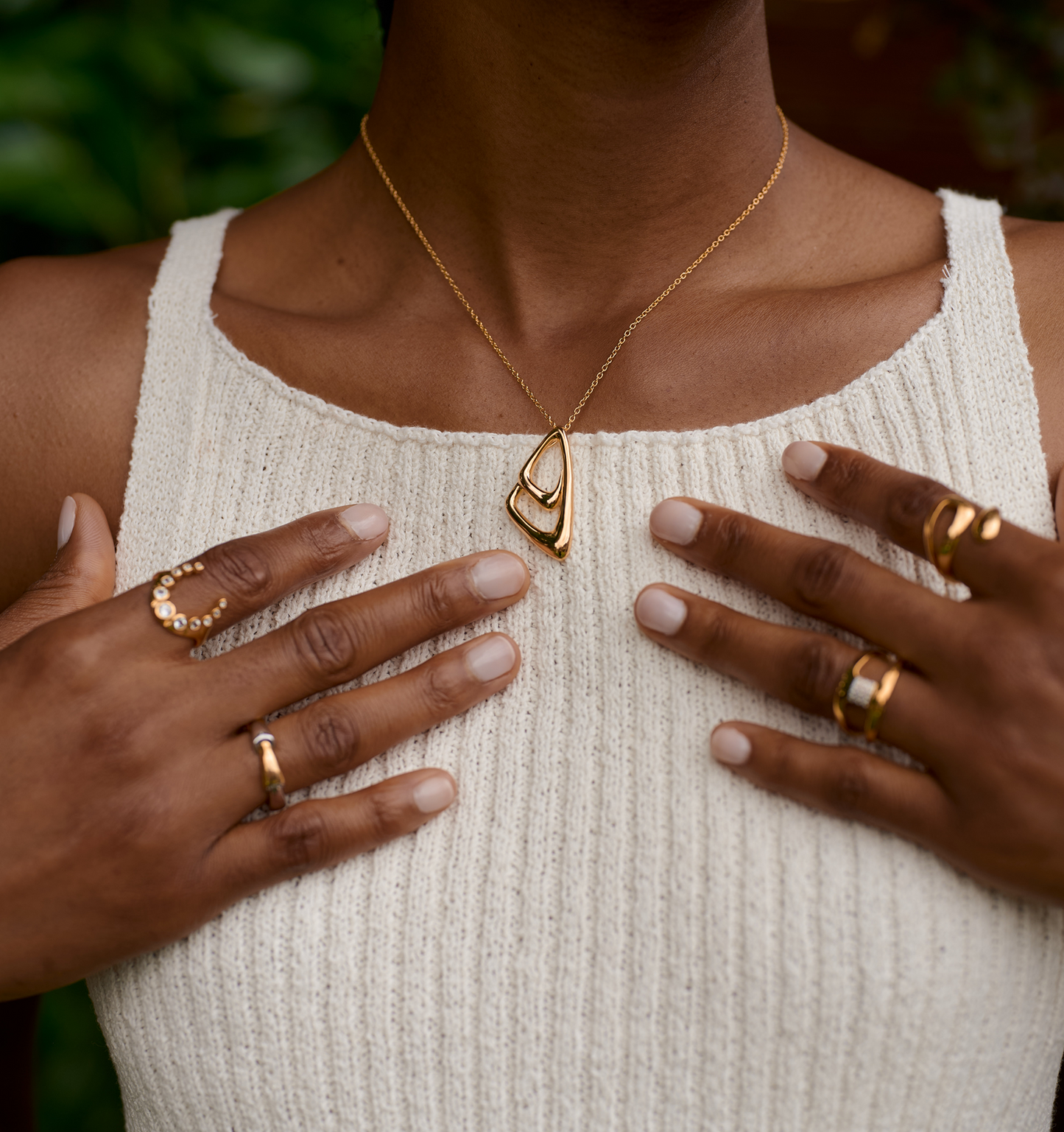 Aavrit Necklace gold geometric pendant on a woman wearing cream knit top and multiple gold rings