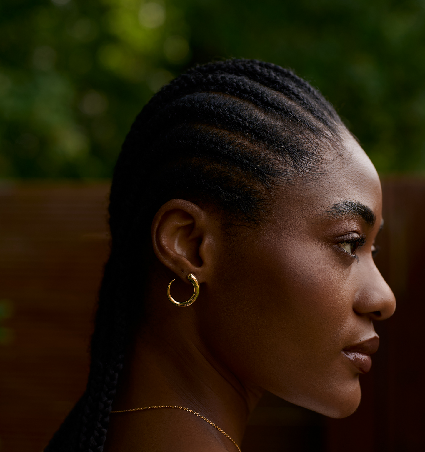 Close-up profile of woman wearing elegant gold Sora earrings with braided hair and natural background