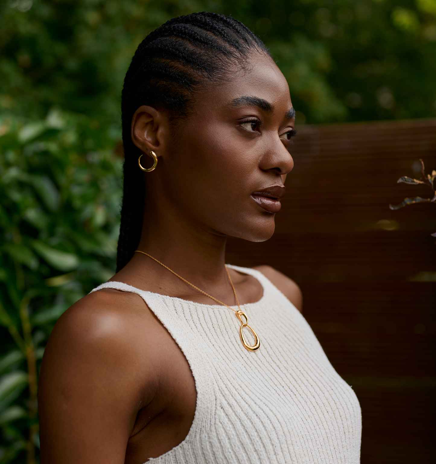 Woman wearing a gold Bindu Necklace with an abstract drop pendant and matching gold hoop earrings outdoors