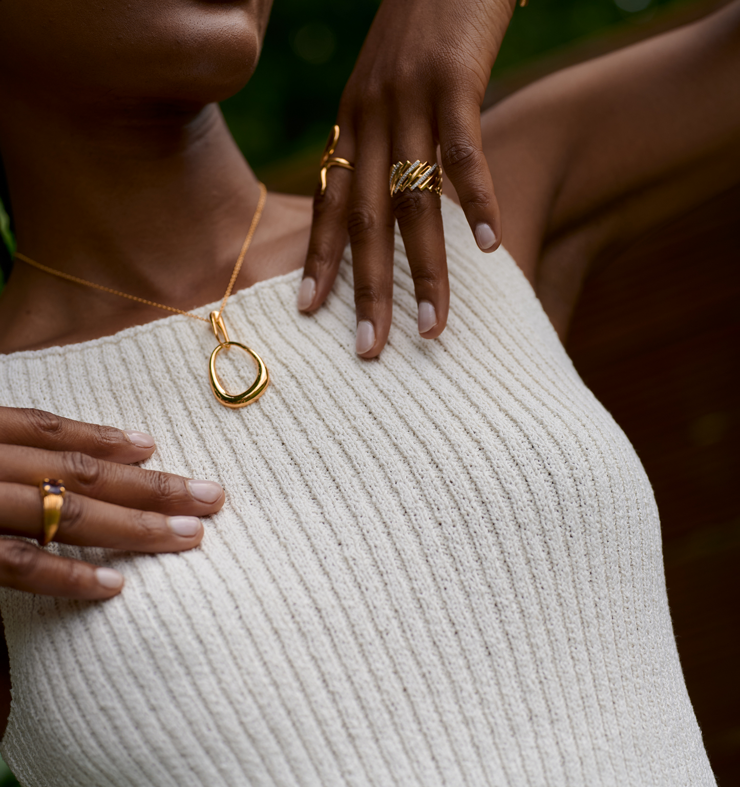 Close-up of a person wearing a sculpted gold Bindu Necklace with matching gold rings on a ribbed white top