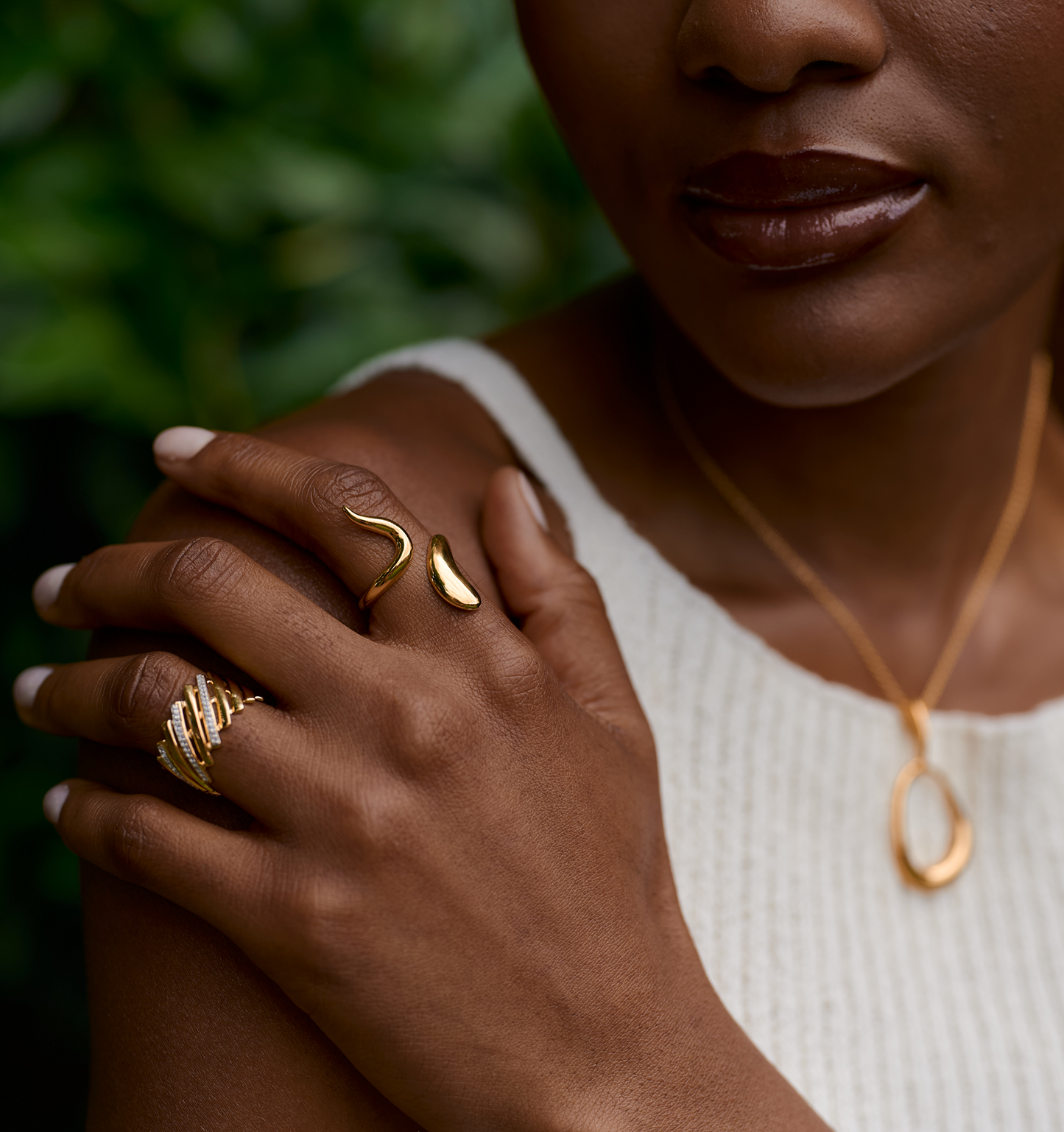 Close-up of a hand wearing a luminous gold Saachi Ring with elegant curved design and complementary gold jewelry.