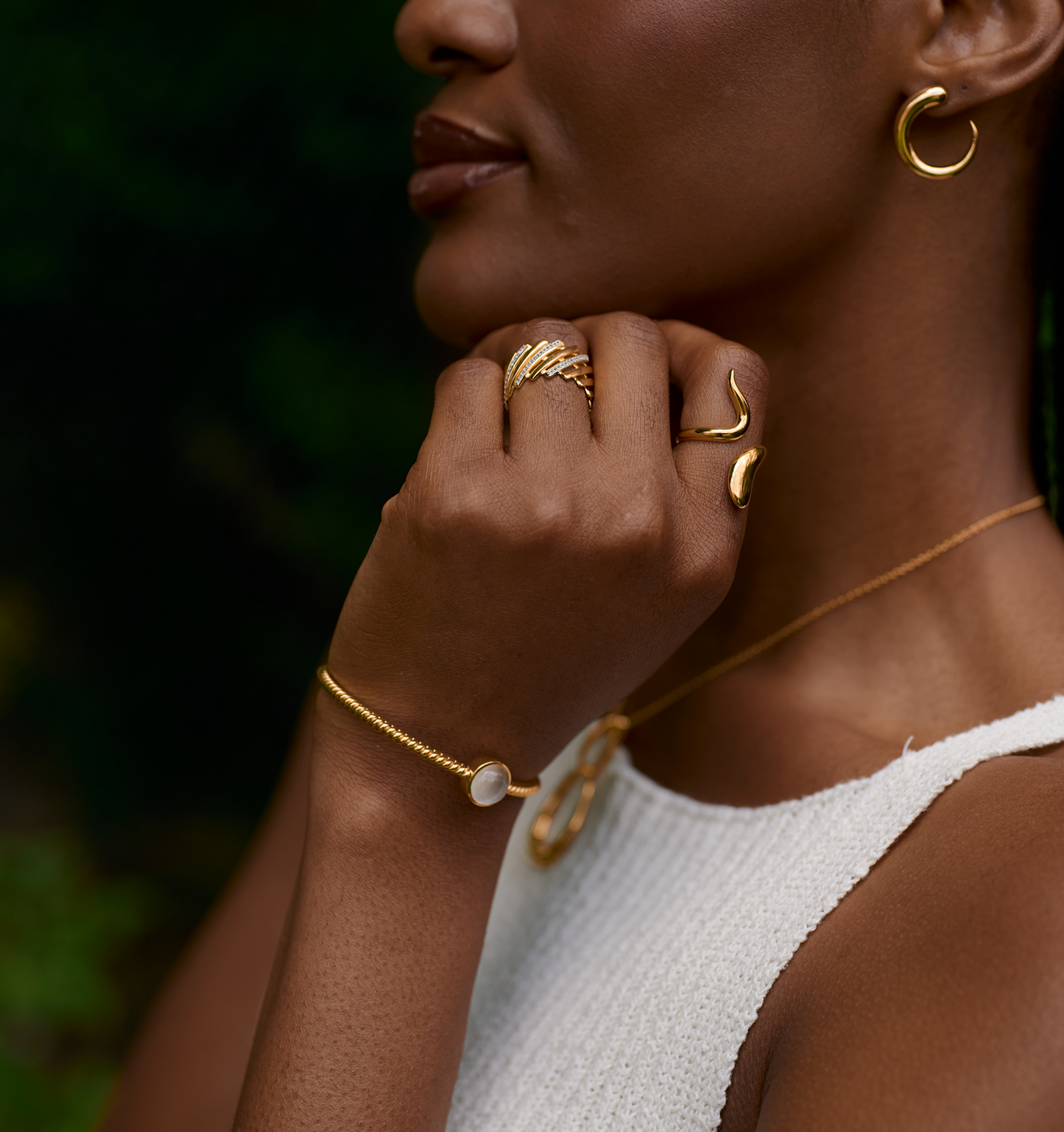 Close-up of woman wearing gold Sora Earrings and matching gold jewelry, featuring elegant sculptural hoop design.