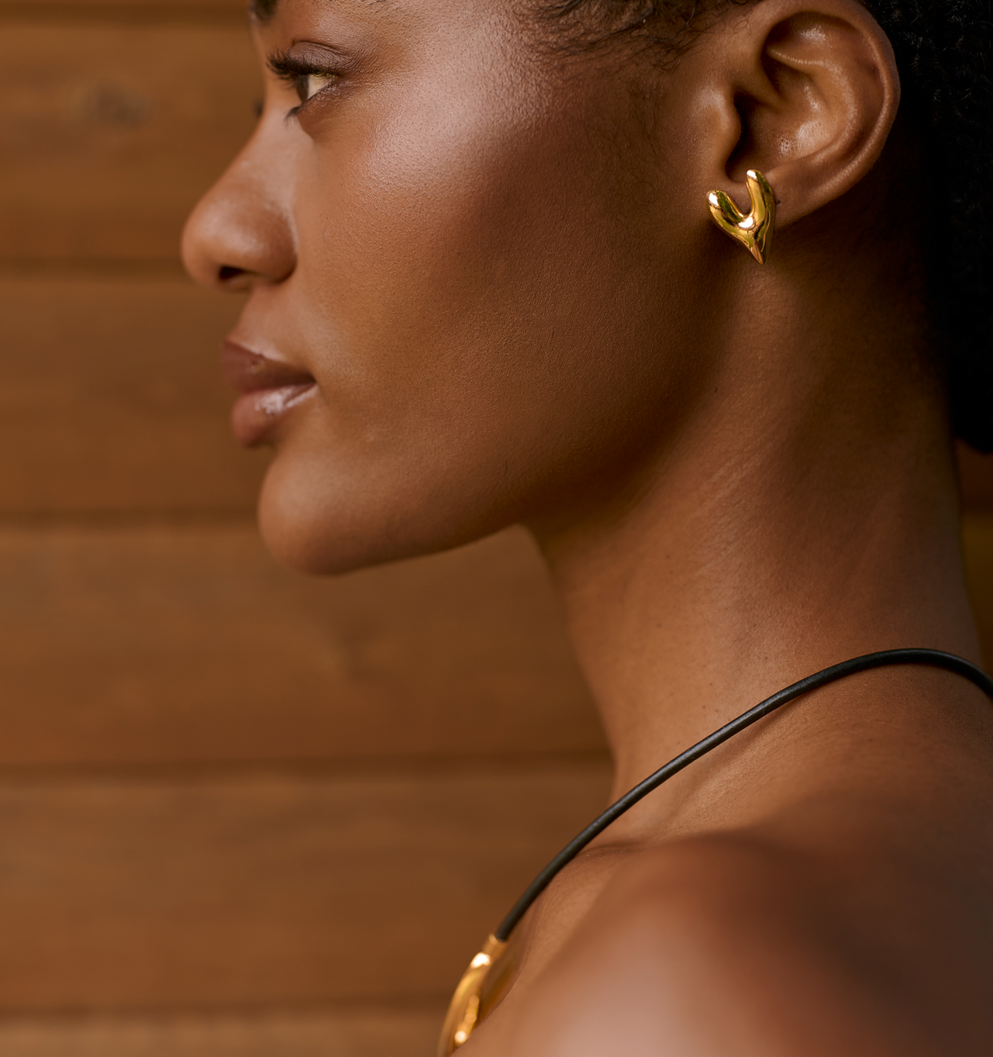 Close-up of a woman wearing gold-toned Avara Earrings with an organic, sculptural heart-shaped design