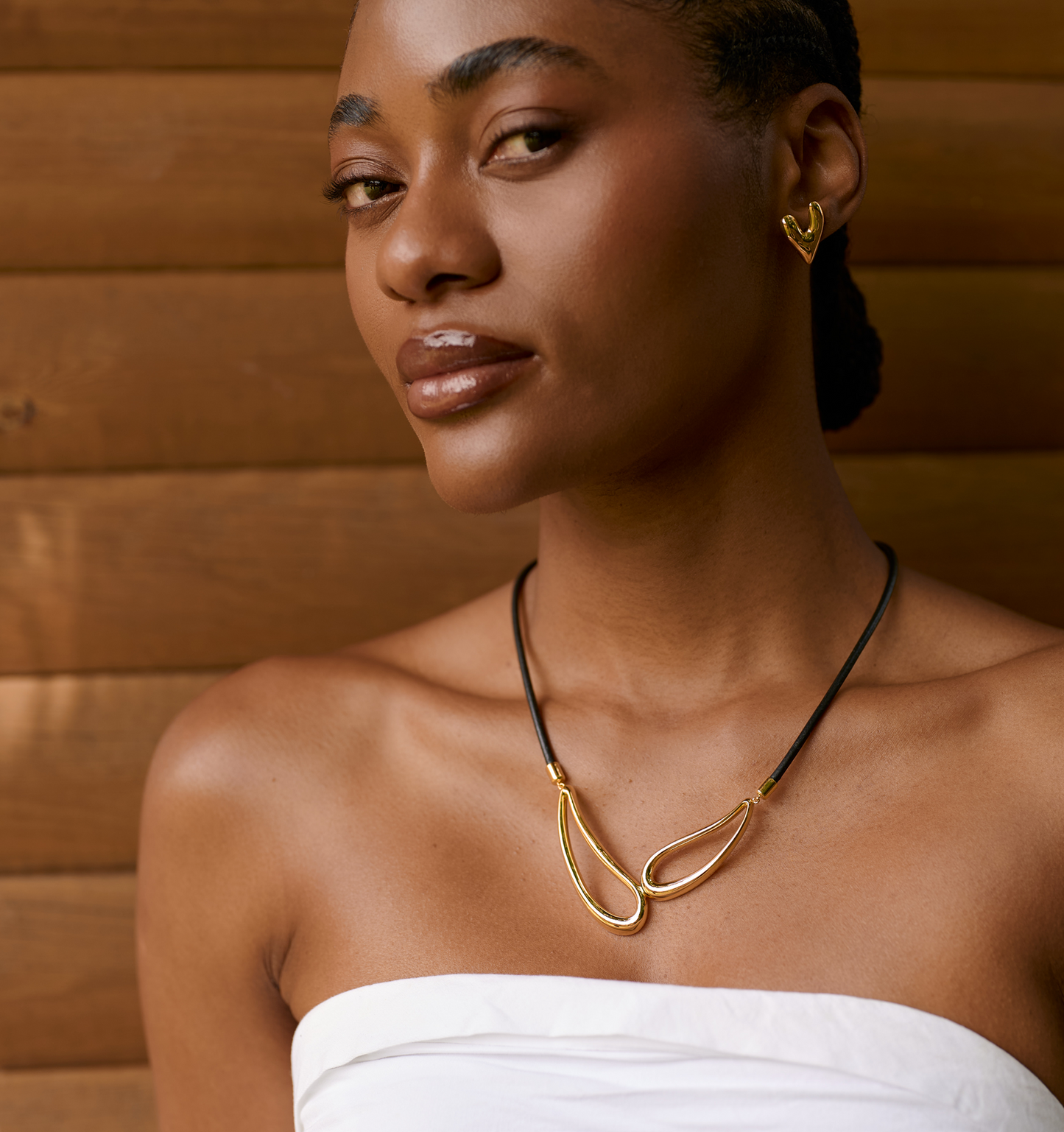 Elegant Saha Necklace with twin sculpted gold forms on black cord worn by woman