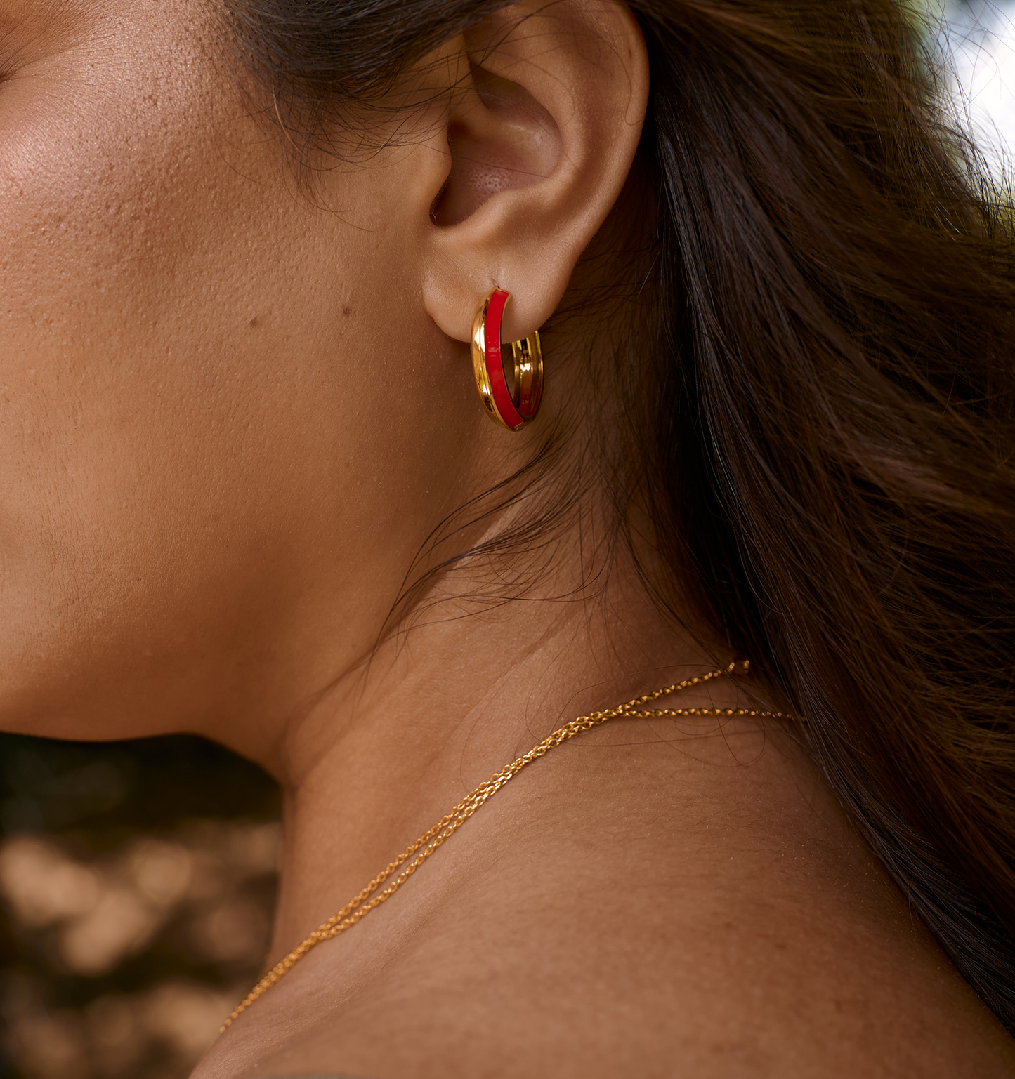 Close-up of a woman wearing a red enamel and gold Rati Hoop earring on her ear