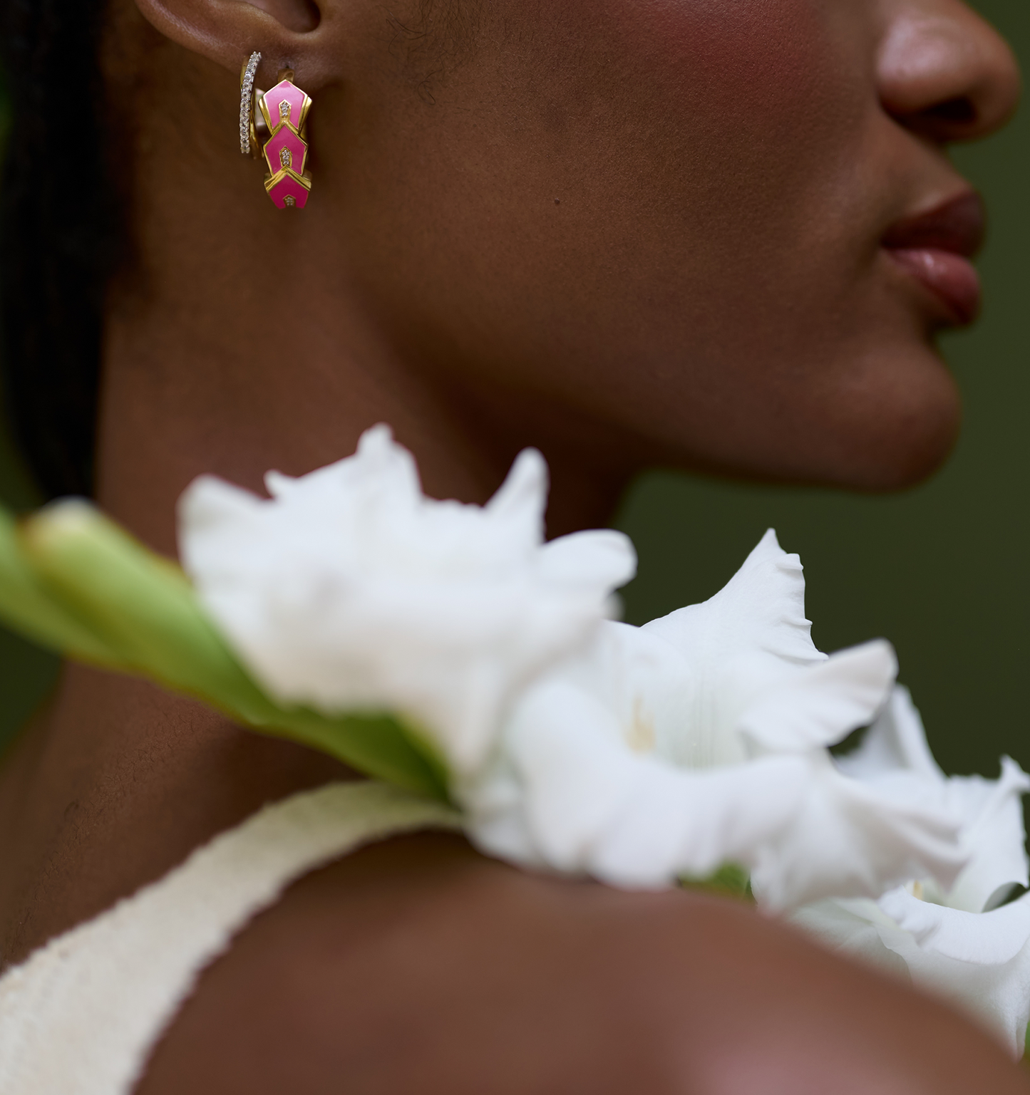 Close-up of Gulzar Petal Dew pink enamel and gold-plated hoop earrings with white topaz on a woman holding white flowers