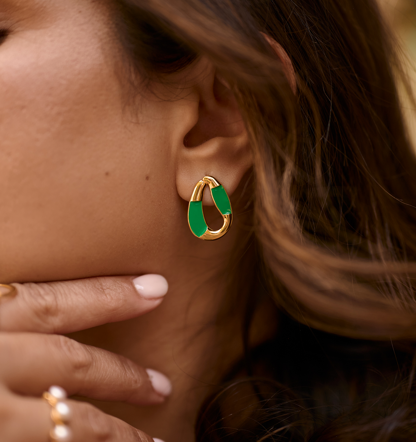 Close-up of a woman's ear wearing a gold and forest green enamel Vana Loop earring