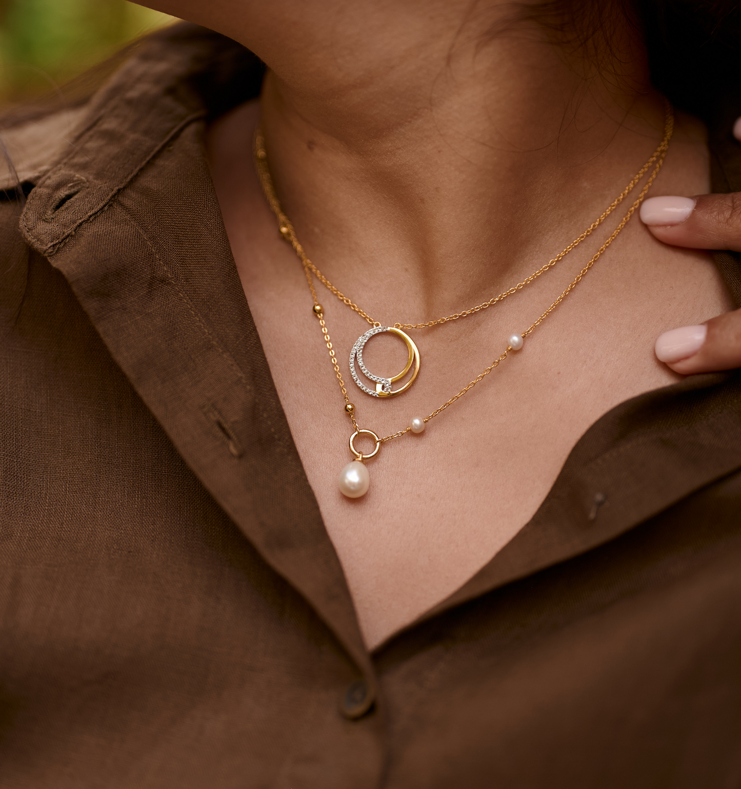 Close-up of Nayra Necklace with gold chains, pearl, and circular pendants worn on neck