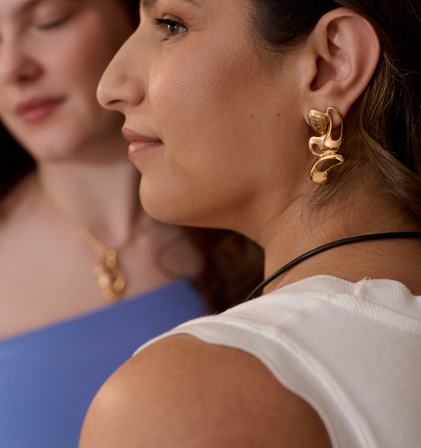 Close-up of radiant gold Nutya earrings on a woman's ear, showcasing fluid and sculptural design inspired by dance movement