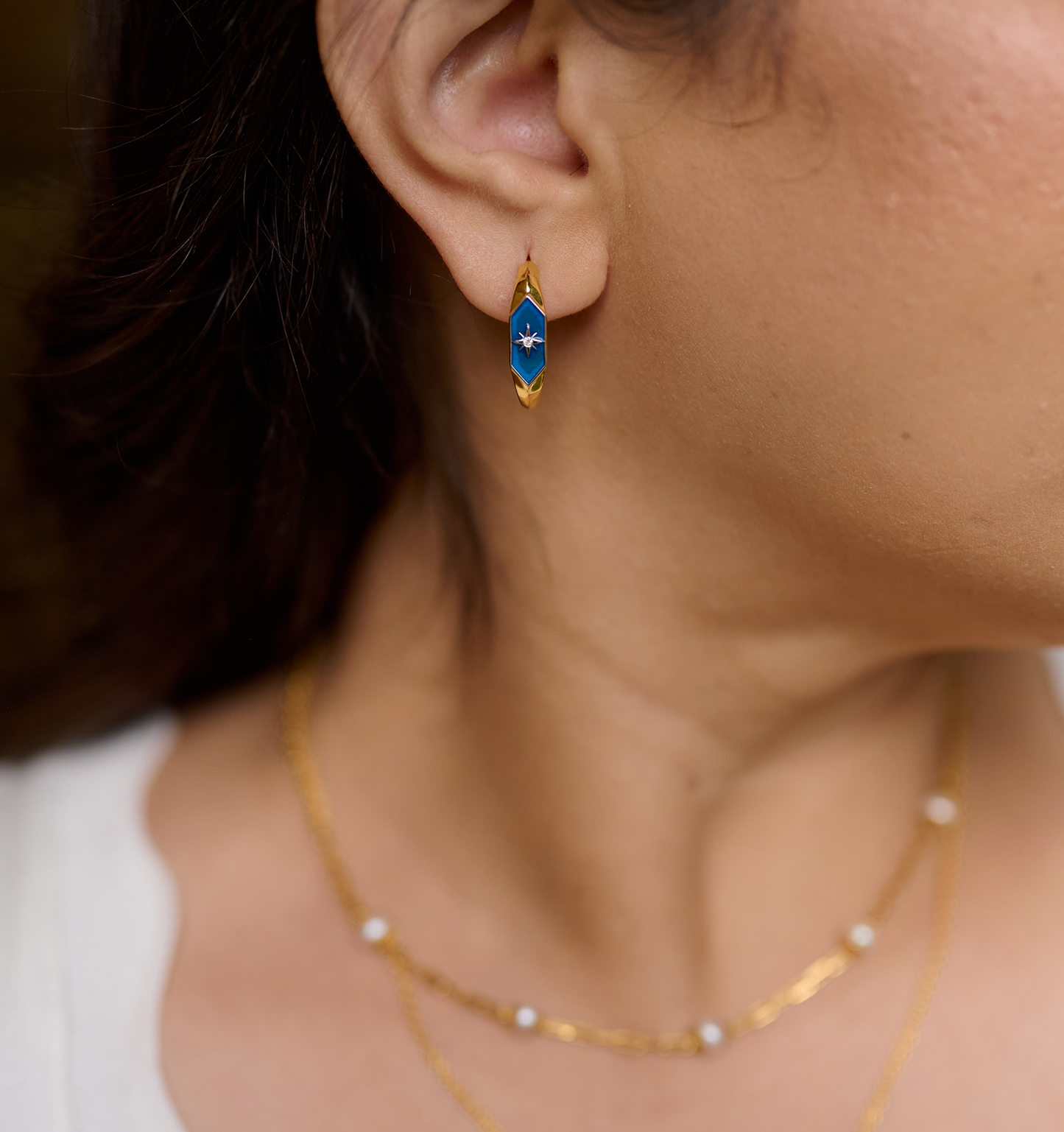Close-up of ear wearing Lumira Hoops gold earrings with blue star design