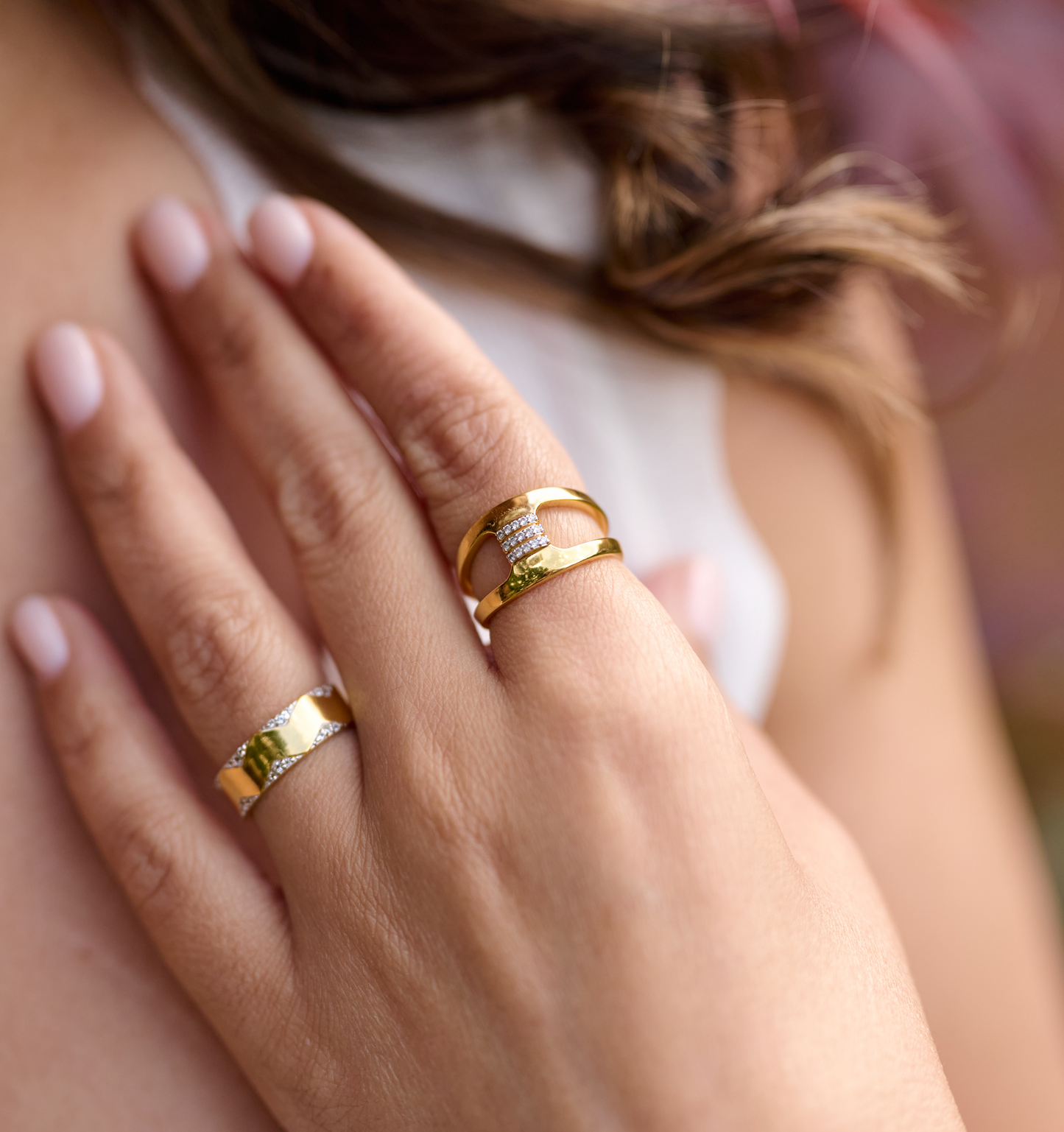 Close-up of hand wearing Setu Ring with two gold arcs connected by white topaz bridge and another gold ring