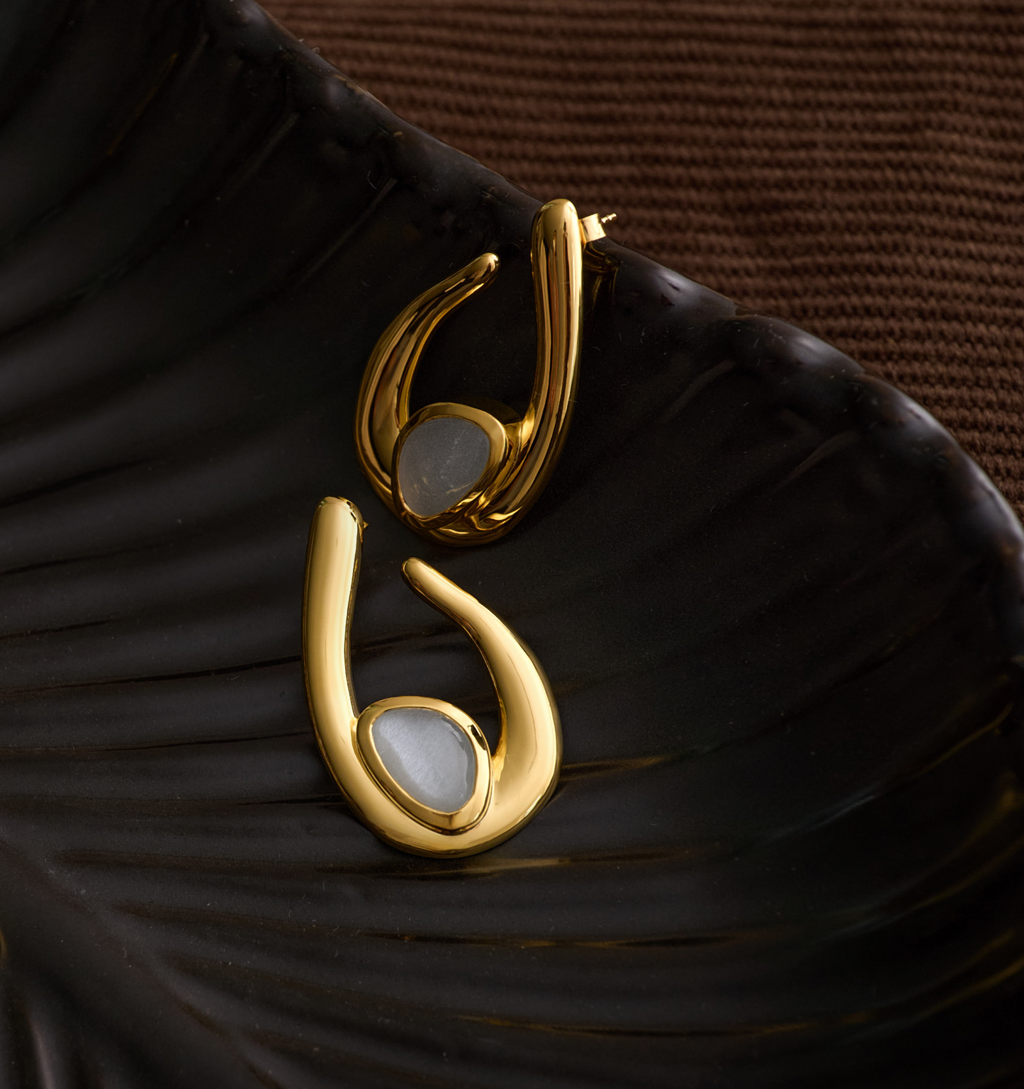 Gold Lunara Earrings with luminous white moonstone on dark textured surface