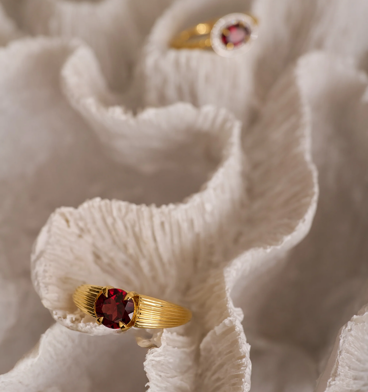 Ishaya Ring with deep red garnet set in bold gold on textured white fabric background