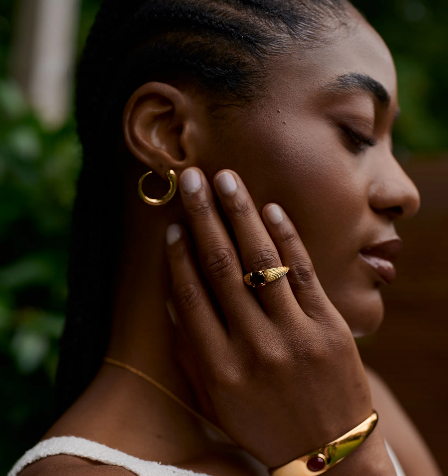 Close-up of woman wearing Ishaya Ring with deep red garnet set in bold gold and matching gold jewelry