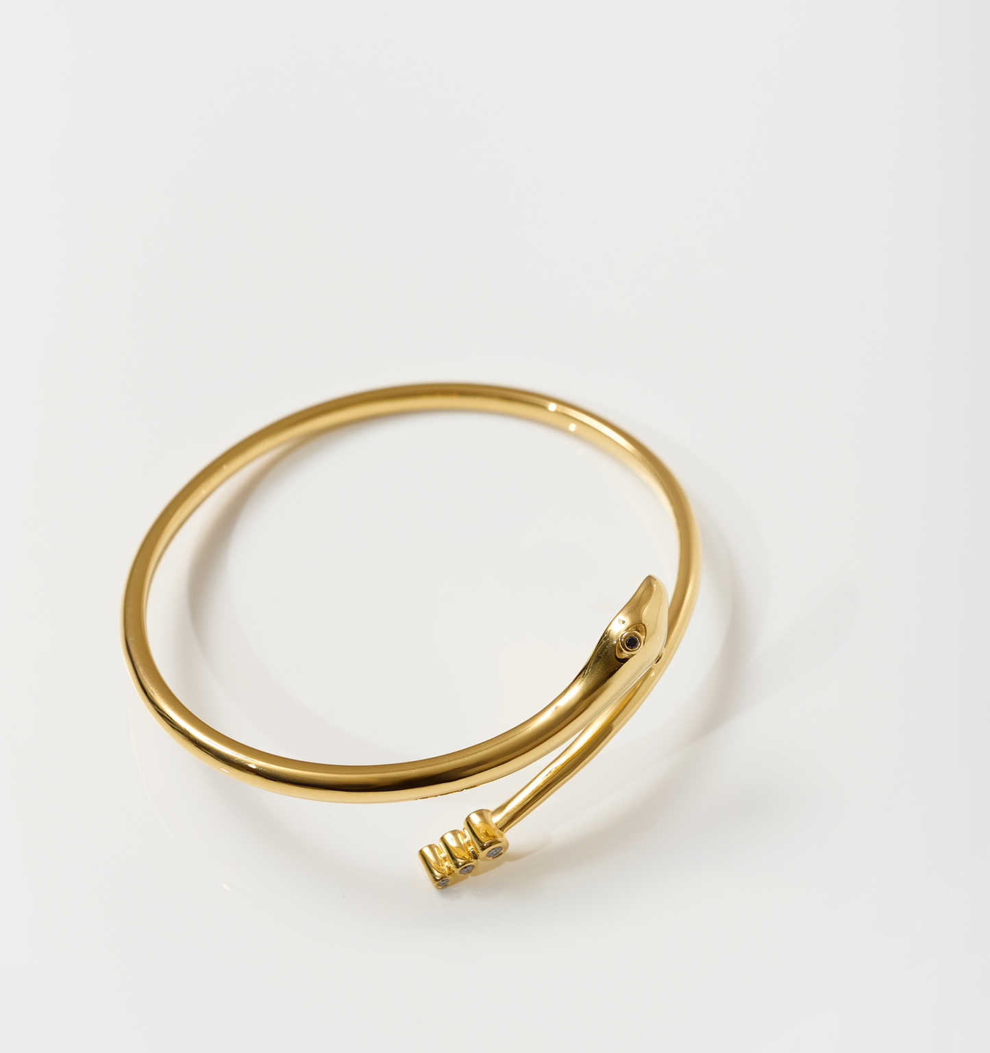 Gold Sarpa Cuff bracelet with serpent design and black spinel eyes on a white background
