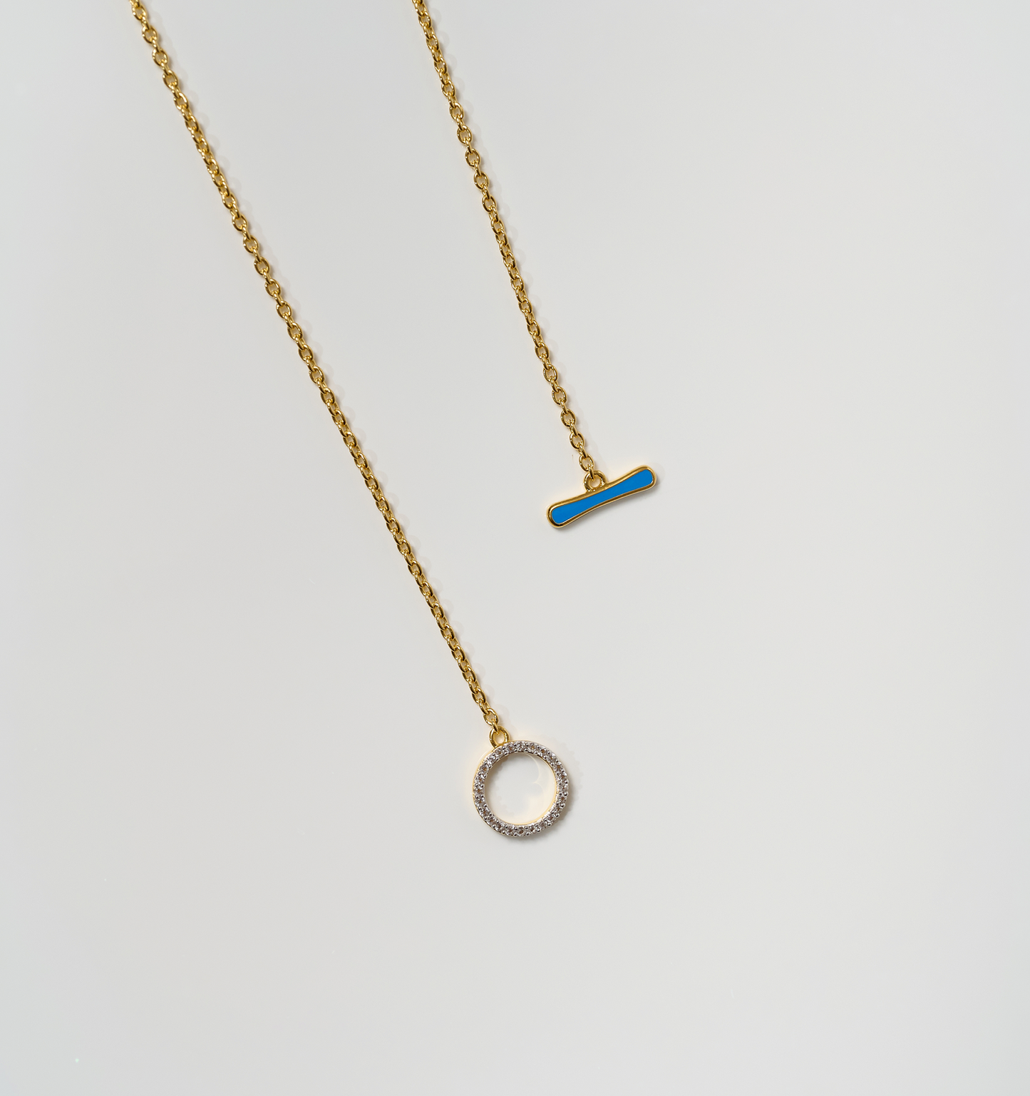 Orya Necklace with white topaz circle and blue bar pendants on gold chains against white background