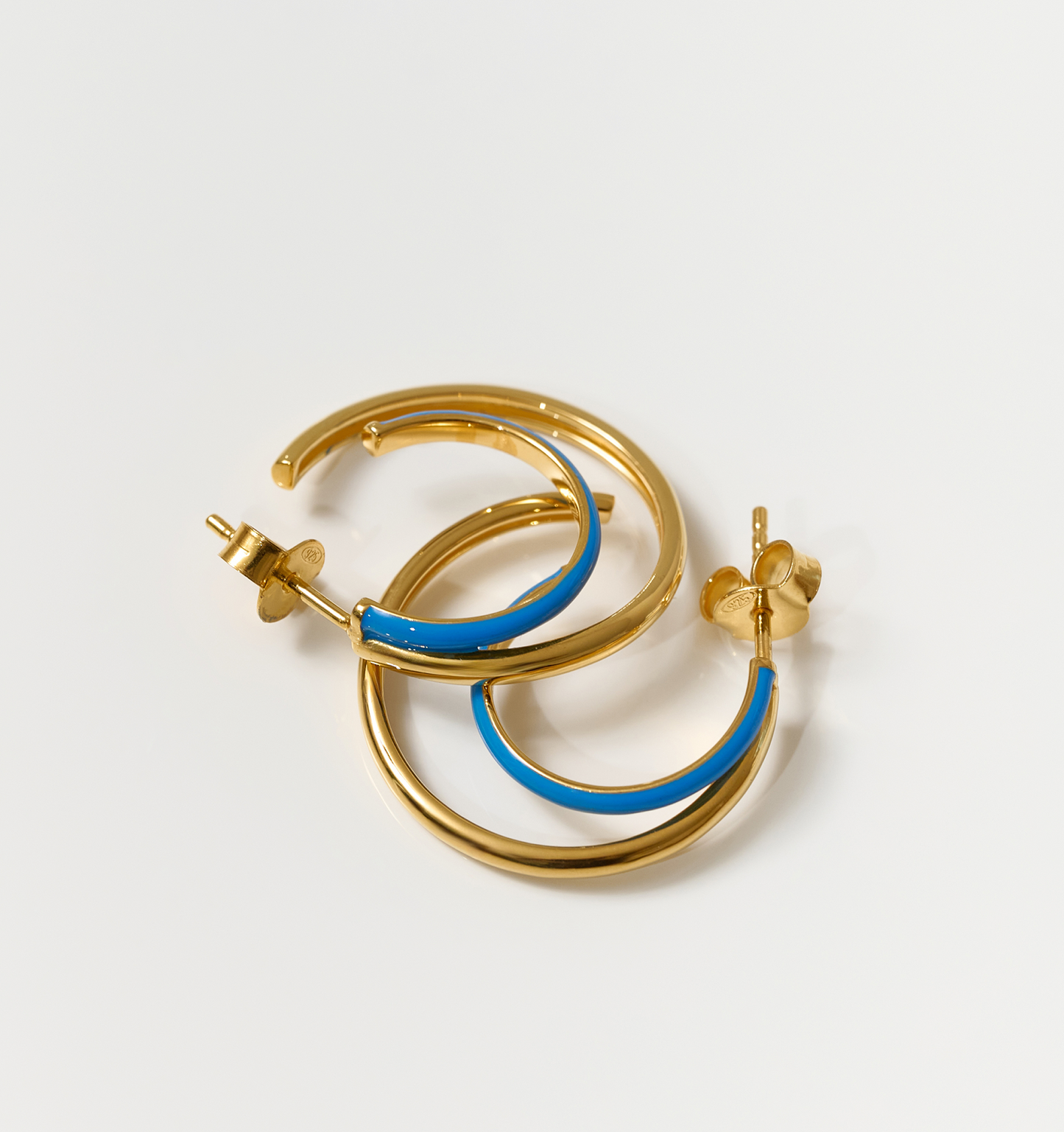 Pair of Soma Hoops earrings with turquoise enamel and polished gold crescent design on white background