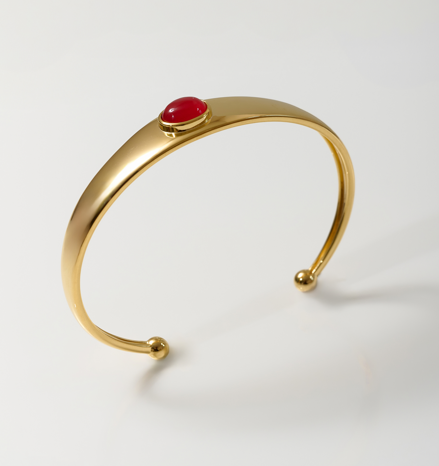 Minimalist gold Dhruva Cuff bracelet with red onyx stone centerpiece on white background