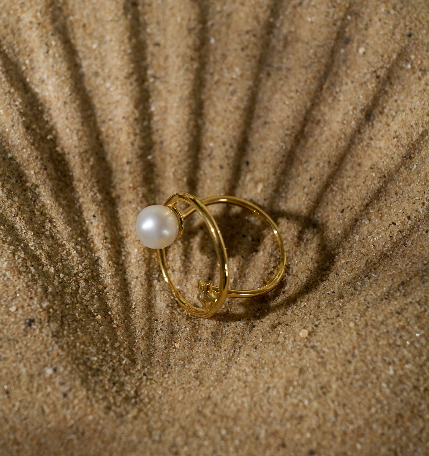 Golden Amishti Ring with pearl and star design on sand background