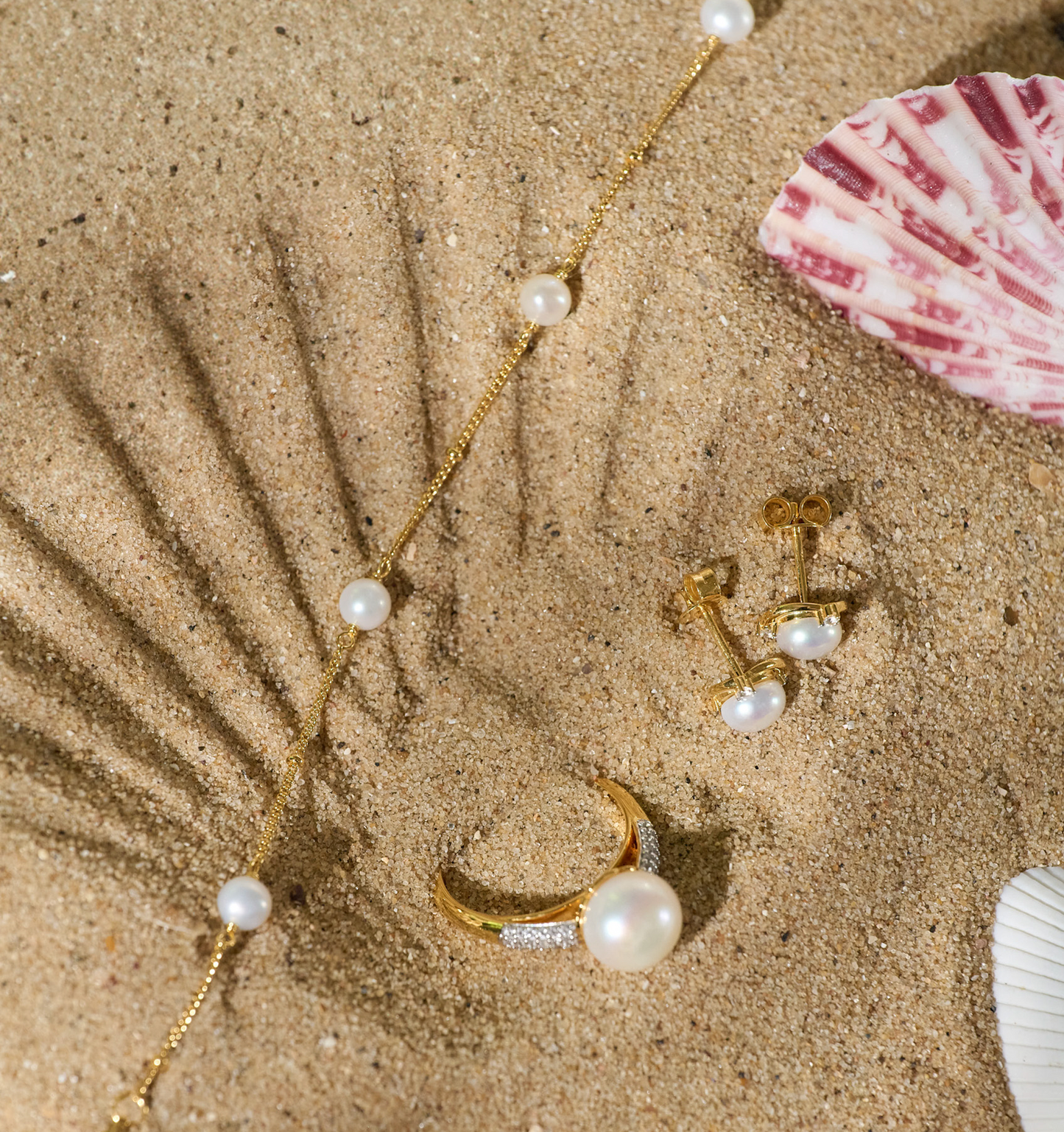 Shanai Bracelet with six pearls on gold chain displayed on sand with matching pearl ring and earrings