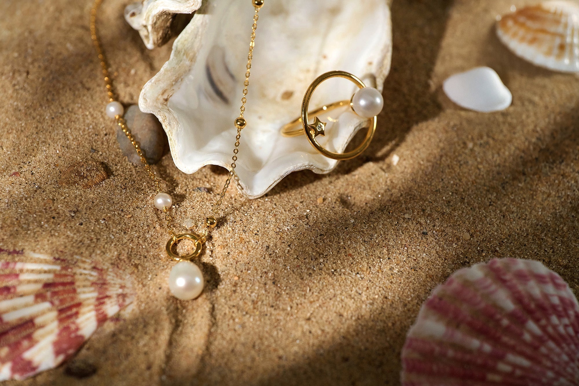 Argha Necklace gold chain with circular pendant and pearl on sandy beach with seashells