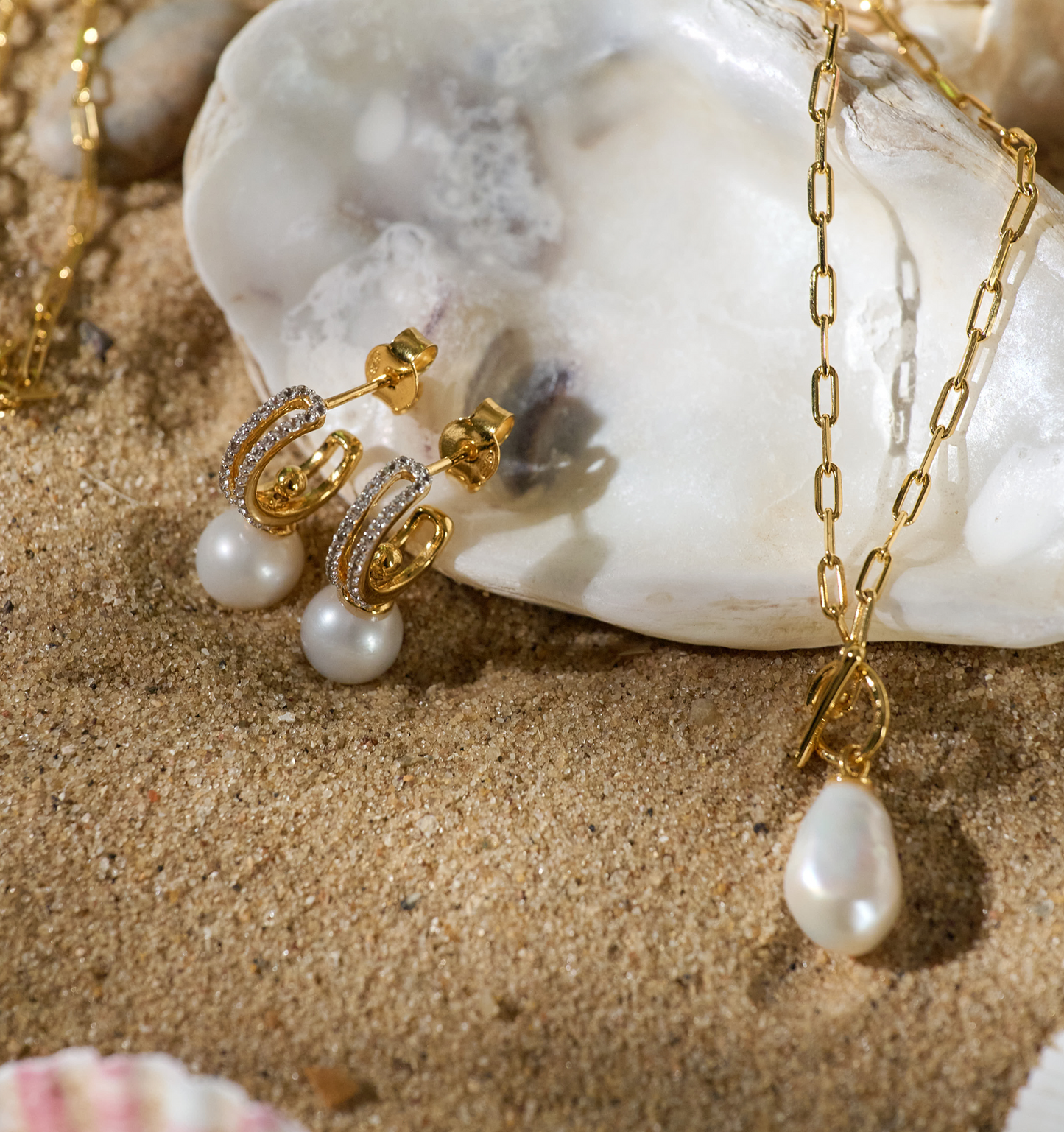 Tarasa Earrings with gold hoops, pearls, and sparkling stars design on sandy background