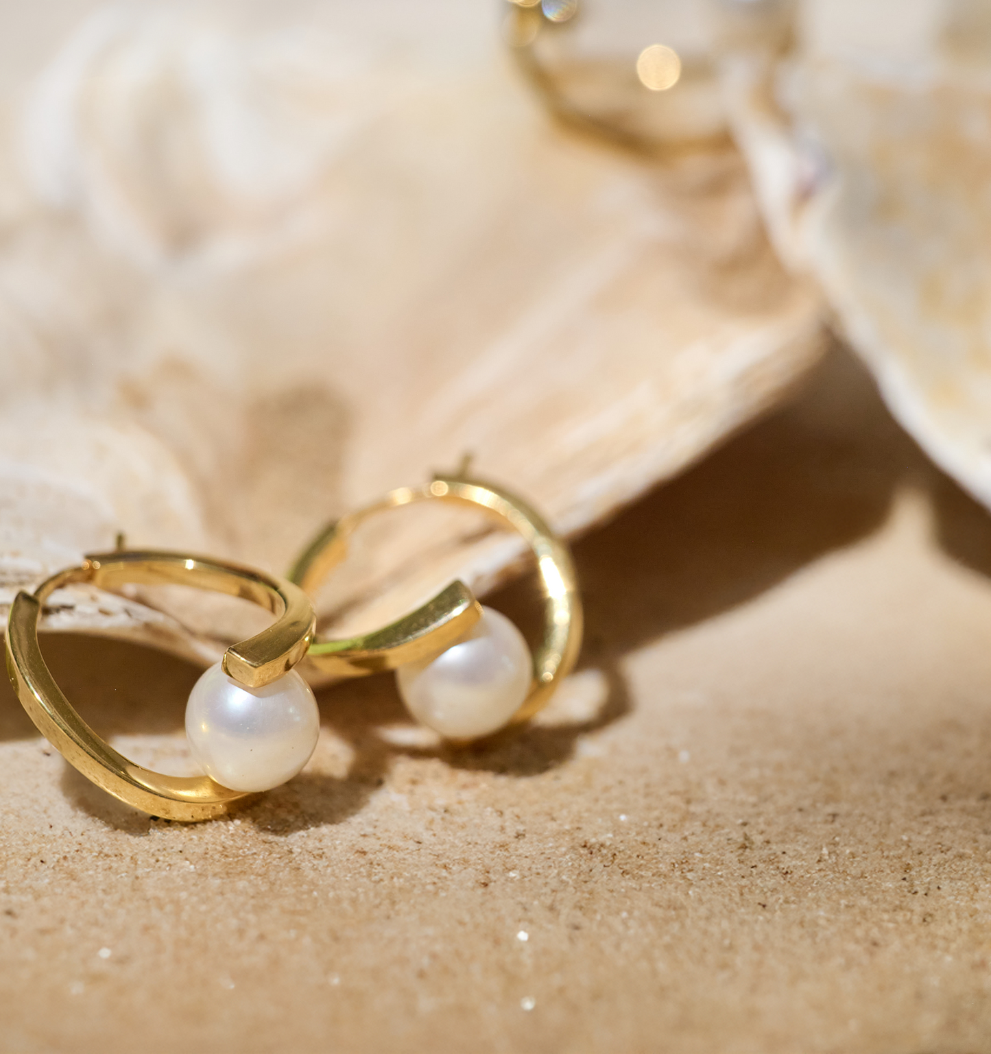 Sharvani Earrings gold hoops with pearls on sandy surface and seashell background