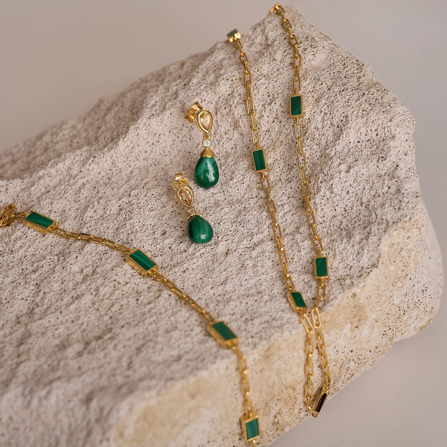 Gold Mann Bracelet with green rectangular stones on textured beige stone background