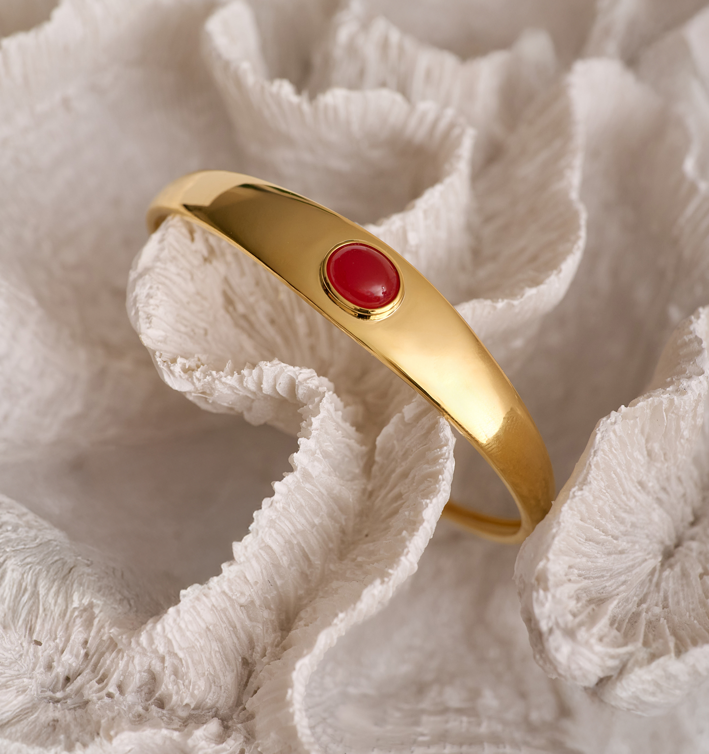 Gold Dhruva Cuff bracelet with red onyx stone on textured white background