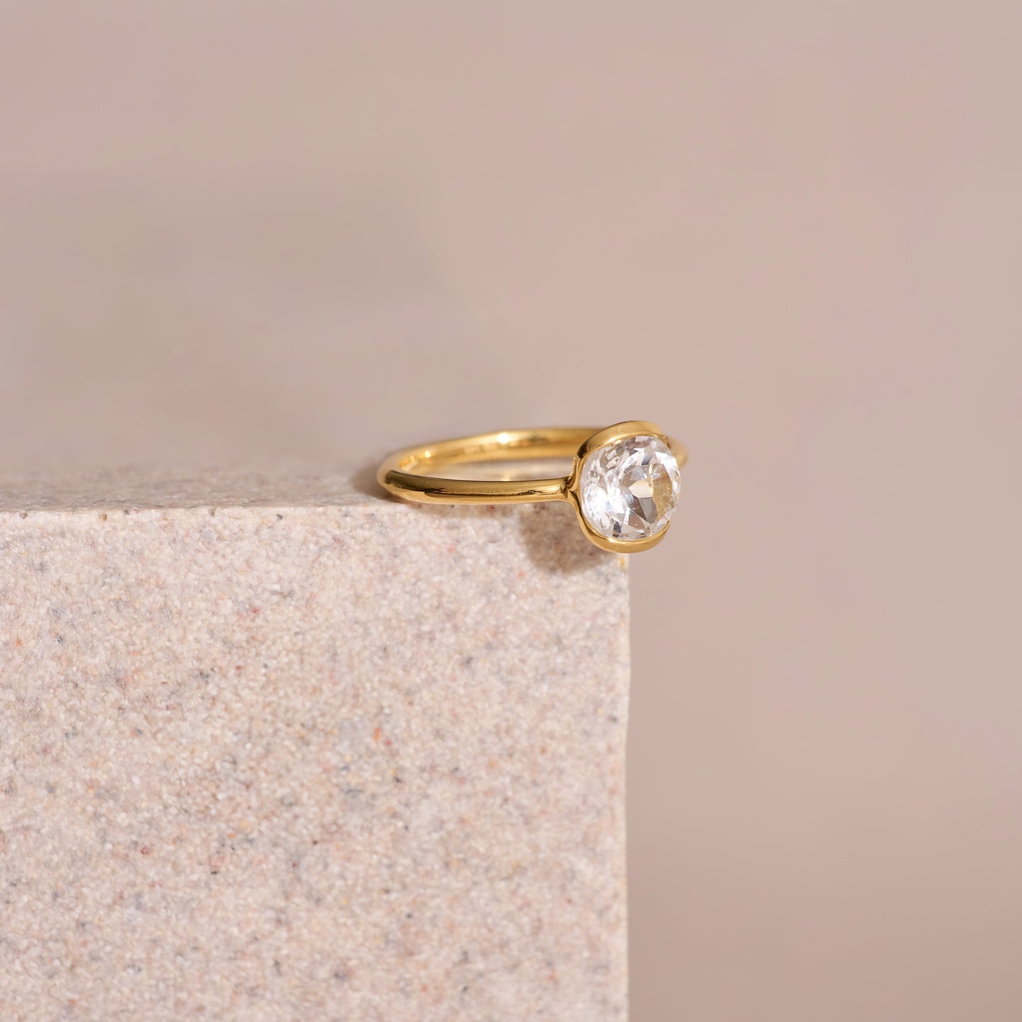 Ruhi Ring with delicate white topaz set in polished gold band on stone surface