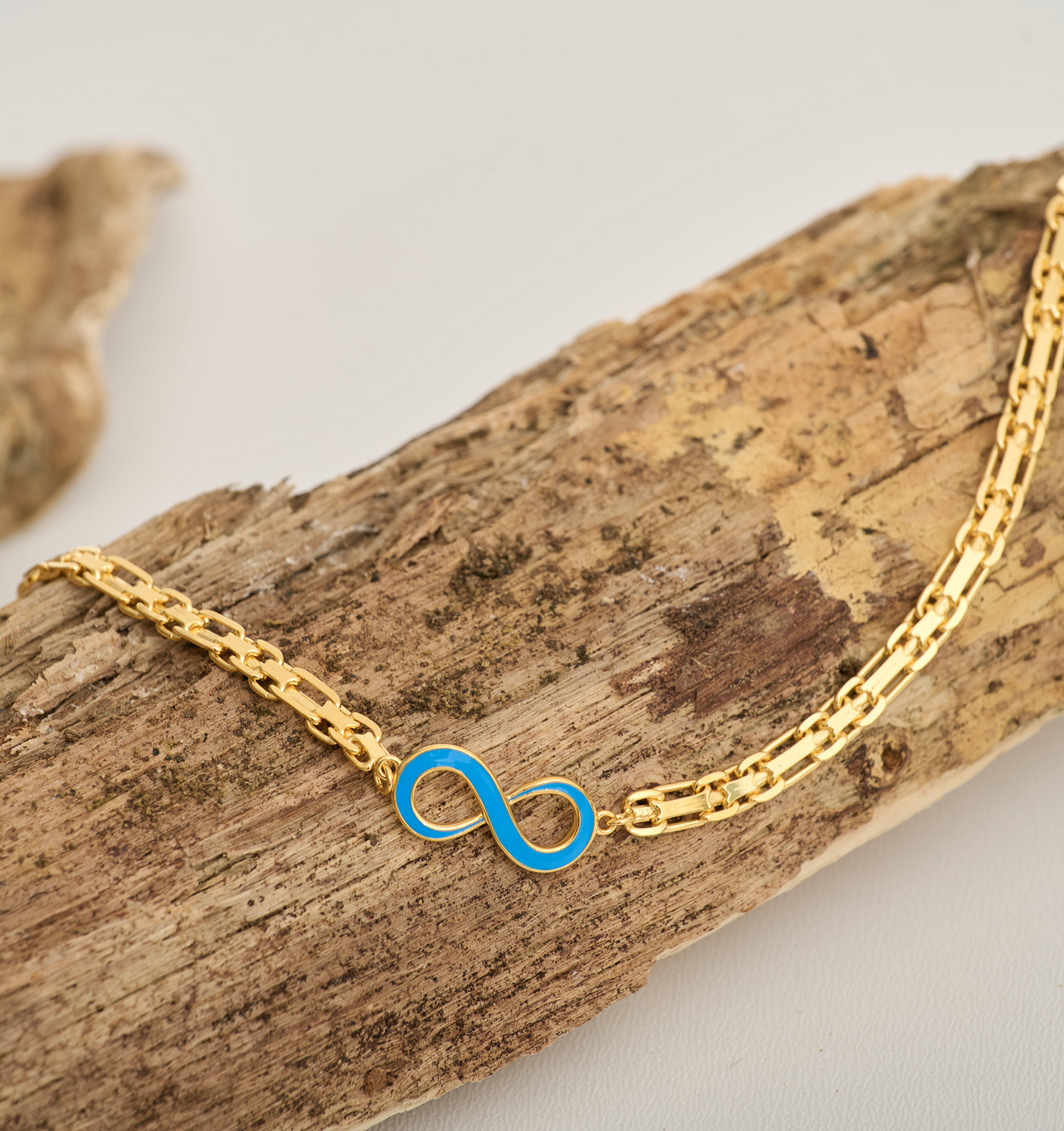 Gold Avaanta Necklace with turquoise enamel infinity pendant on wooden surface