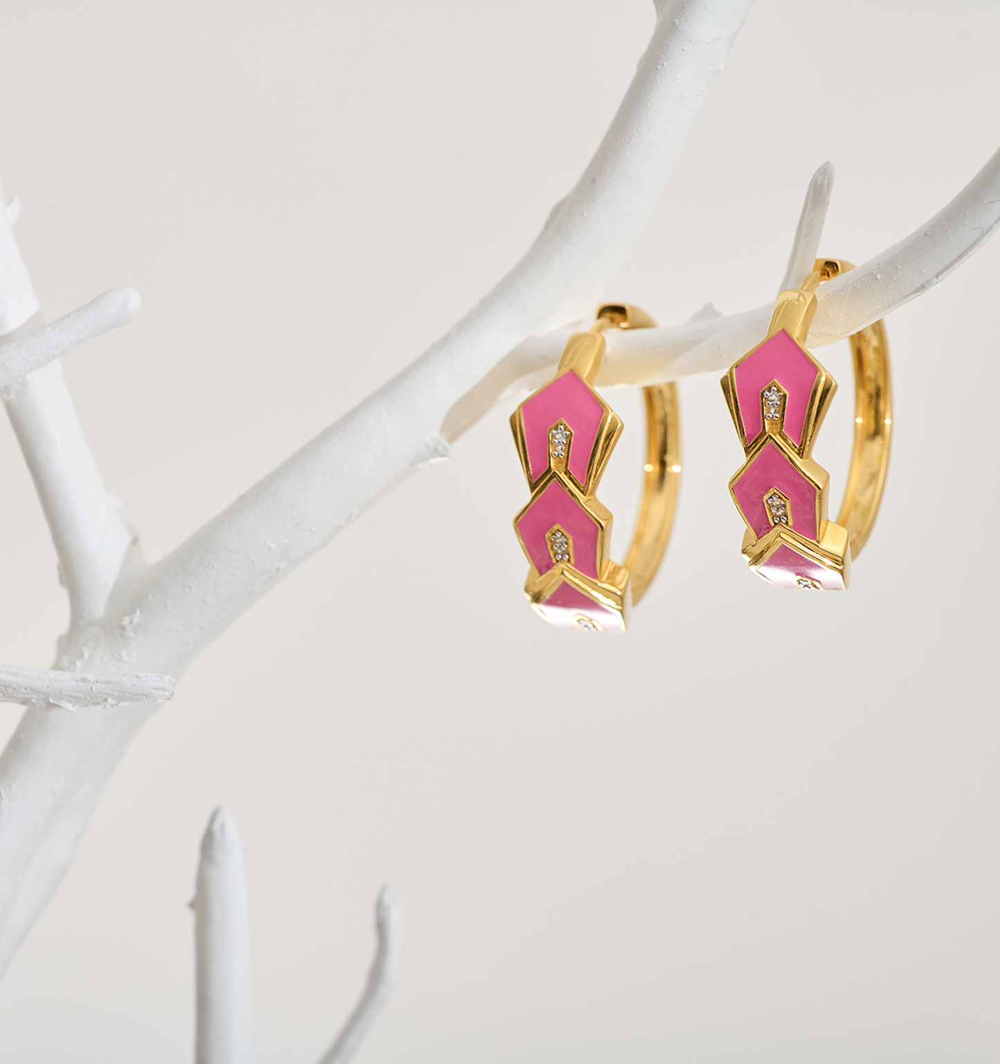 Gulzar Petal Dew gold-plated hoops with pink enamel petals and white topaz accents hanging on white branch