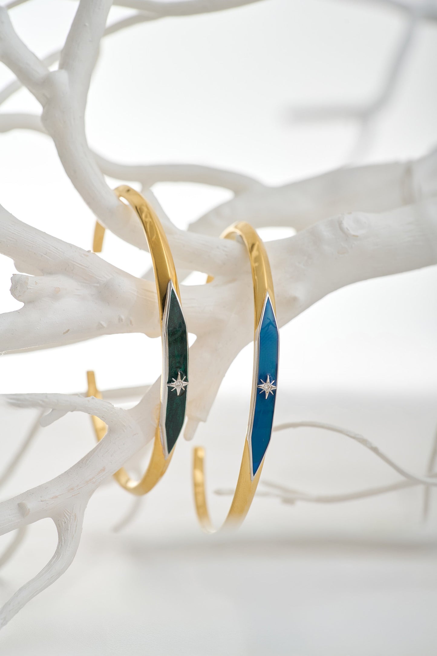 Two Naksha Cuff bracelets with enamel and diamond accents displayed on white branches