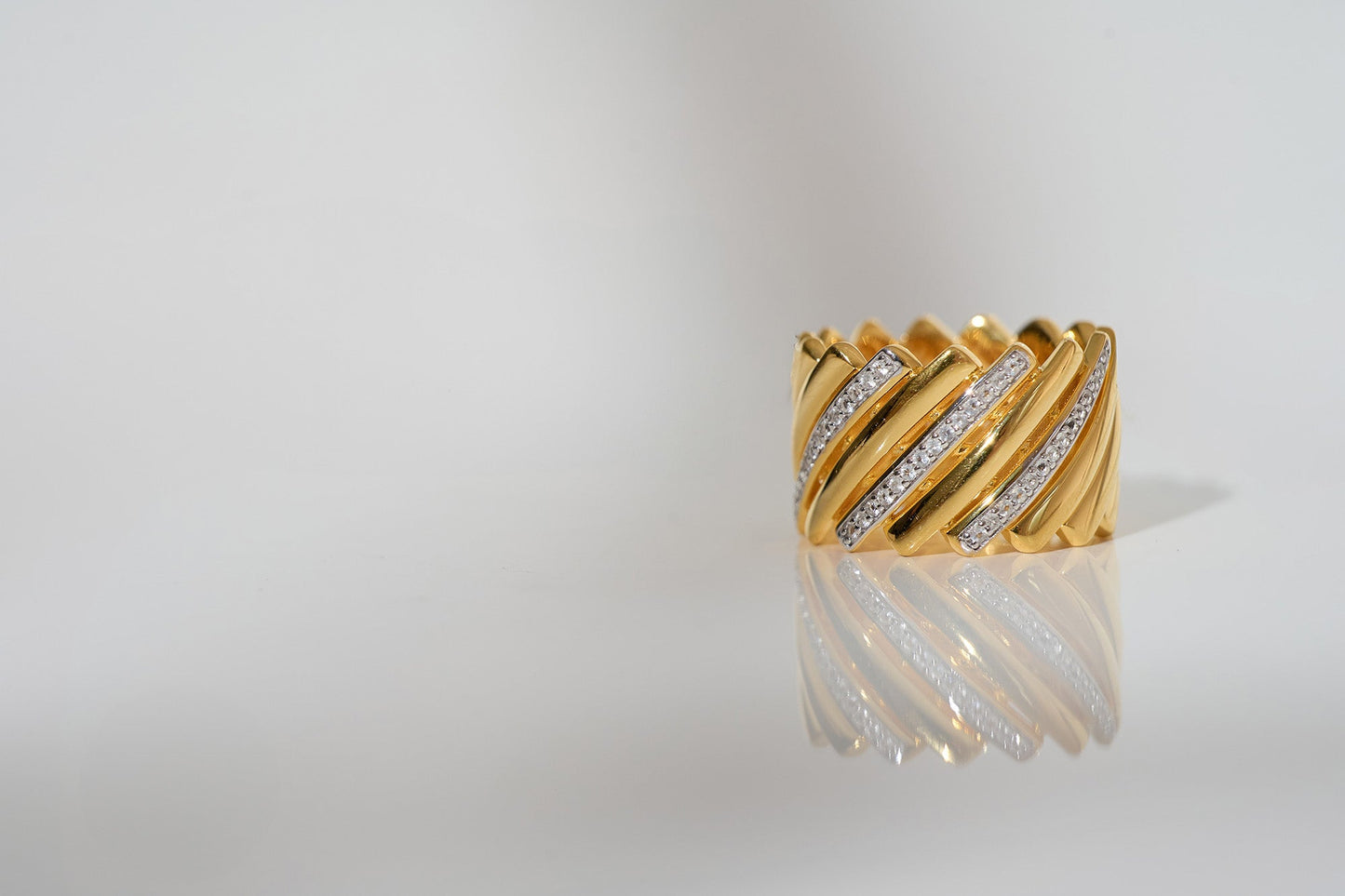 Gold Reya Ring with chevron curves and white topaz stones reflecting on a white surface