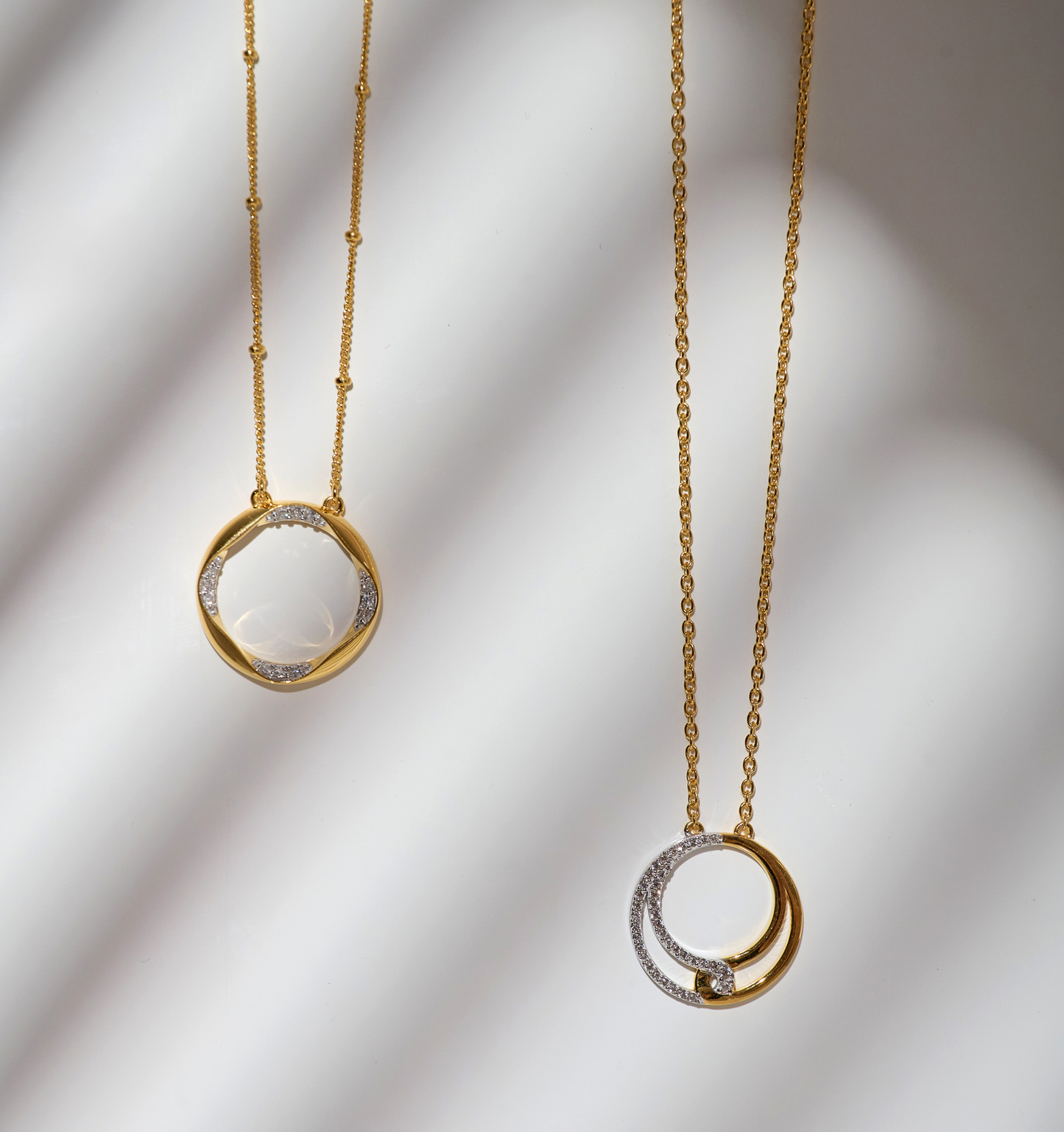 Two elegant Nayra Necklaces with gold and diamond circular pendants on delicate chains