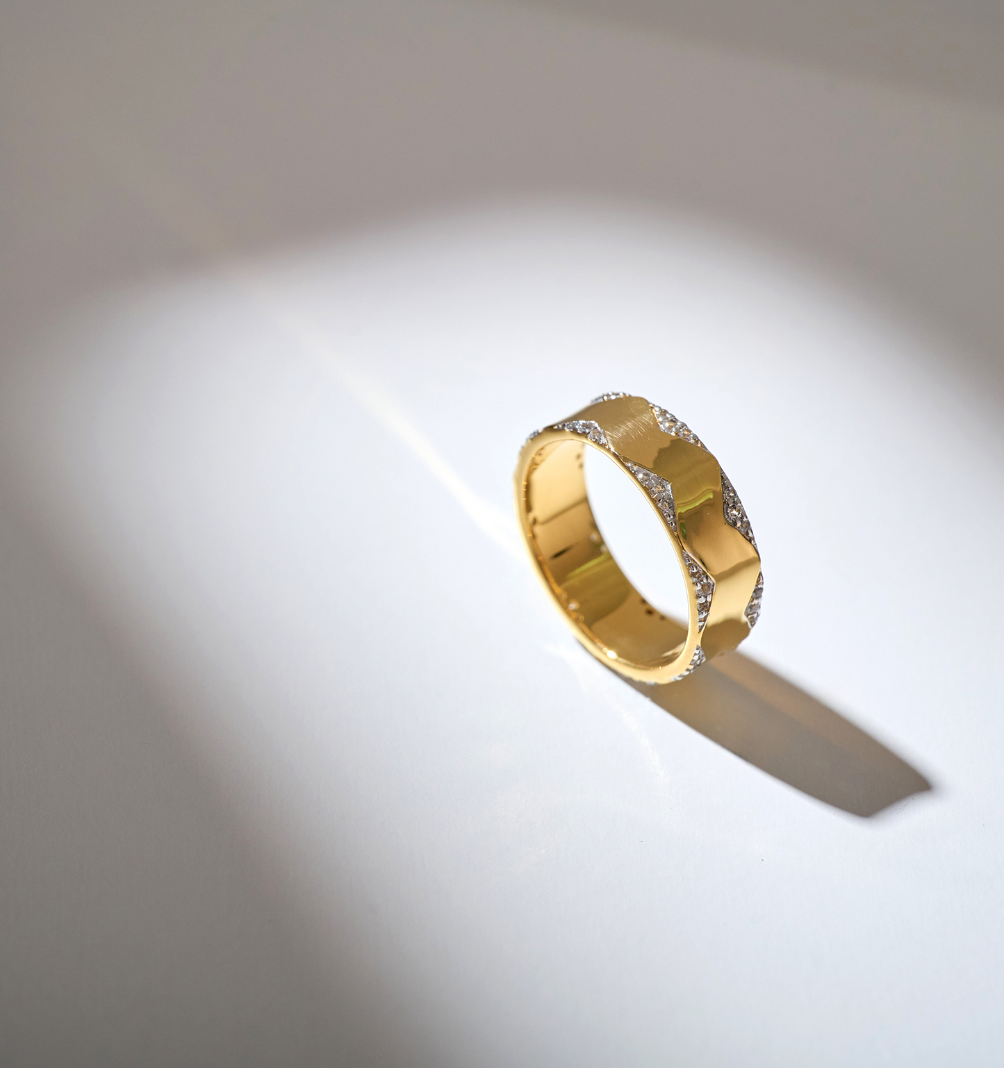 Vedya Ring gold band with sculpted curves and white topaz accents illuminated by light on a white background