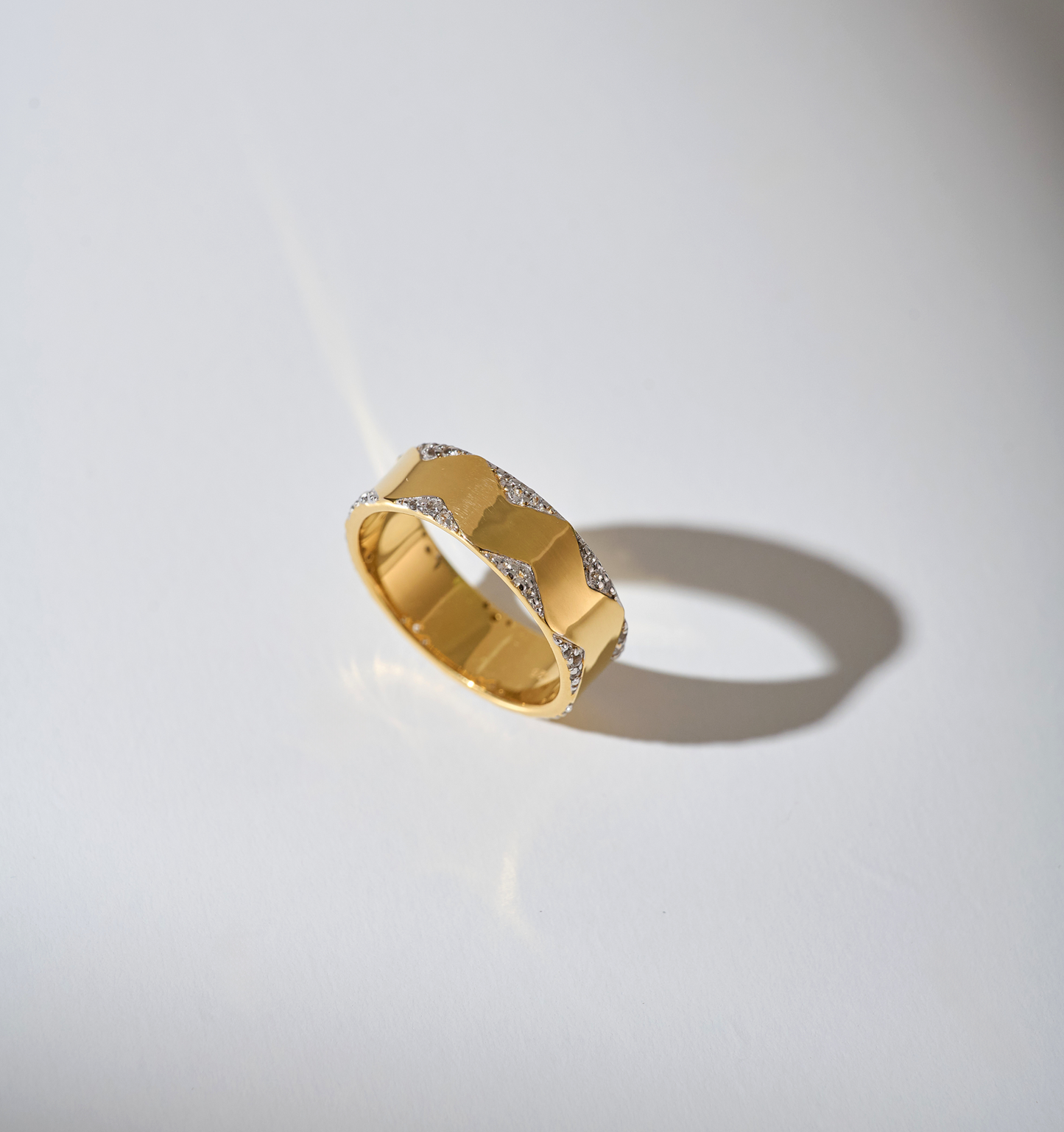 Vedya Ring gold band with sculpted curves and white topaz accents reflecting light on a white surface