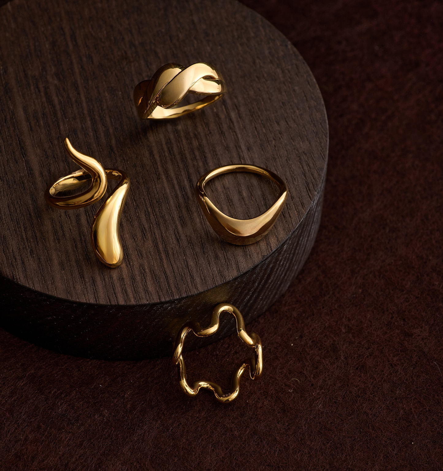 Gold Neer Ring with a smooth, flowing design inspired by water ripples on a dark wooden surface