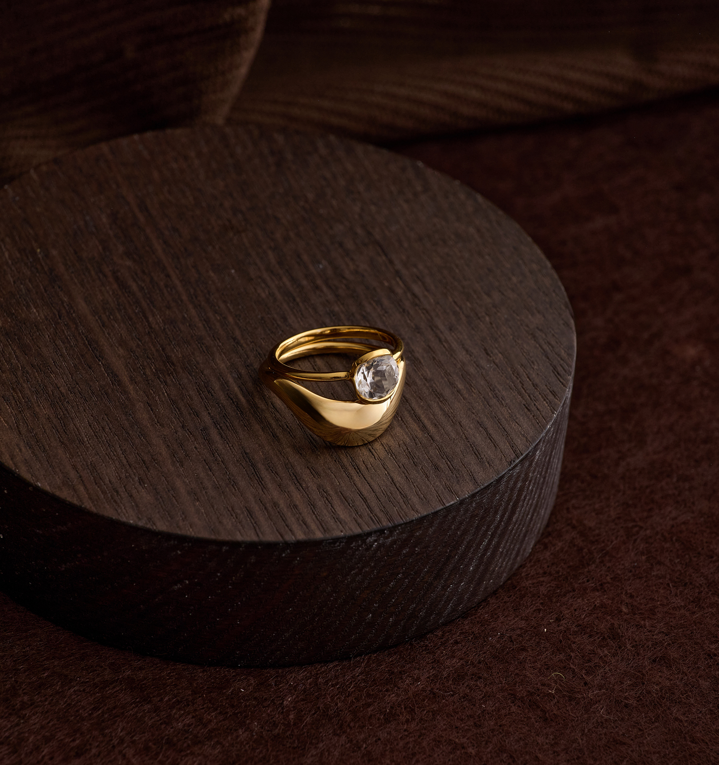 Gold Alav Ring with a single clear gemstone on a dark wooden display stand