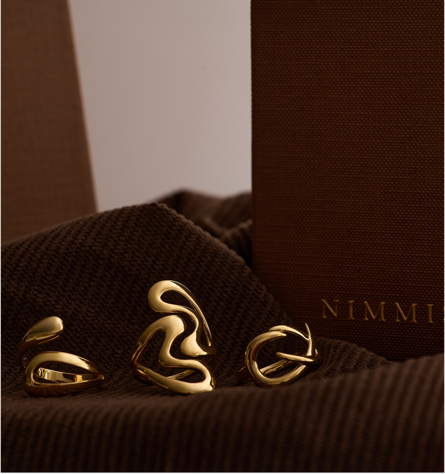 Elegant gold Karvat Ring with fluid, sculpted curves symbolizing tension and grace on a textured brown background