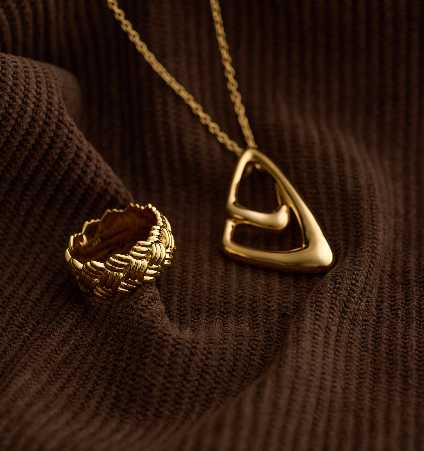 Gold Kaari Ring with intricate woven design displayed on brown fabric with matching gold pendant necklace
