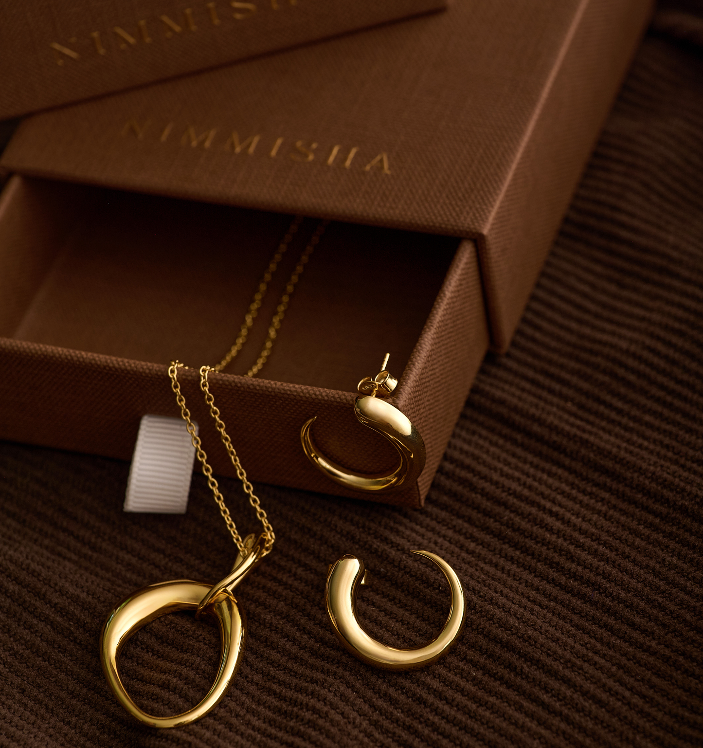 Bindu Necklace sculpted gold drop pendant with matching gold earrings on brown textured background
