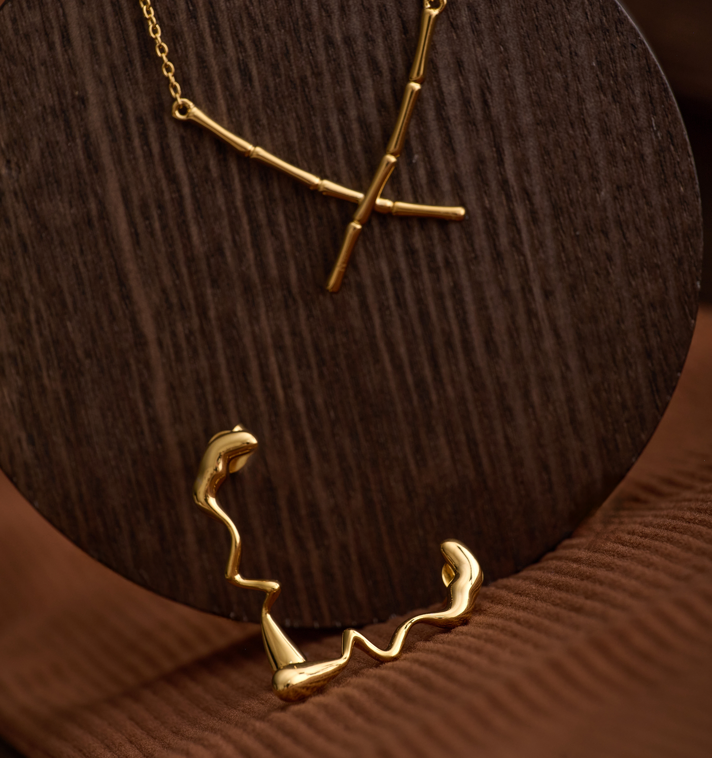 Gold Caia Earrings with fluid, wavy design inspired by flame movement on dark wooden background